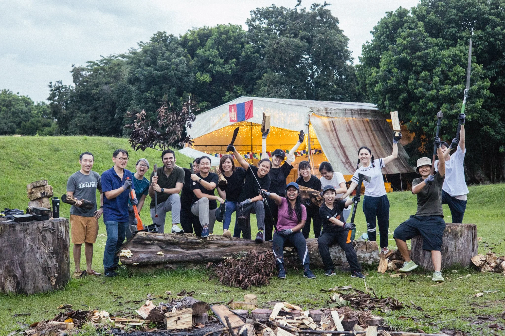 A Singapore corporate team holding saws and axes after an outdoor team bonding challenge on Pulau Ubin.