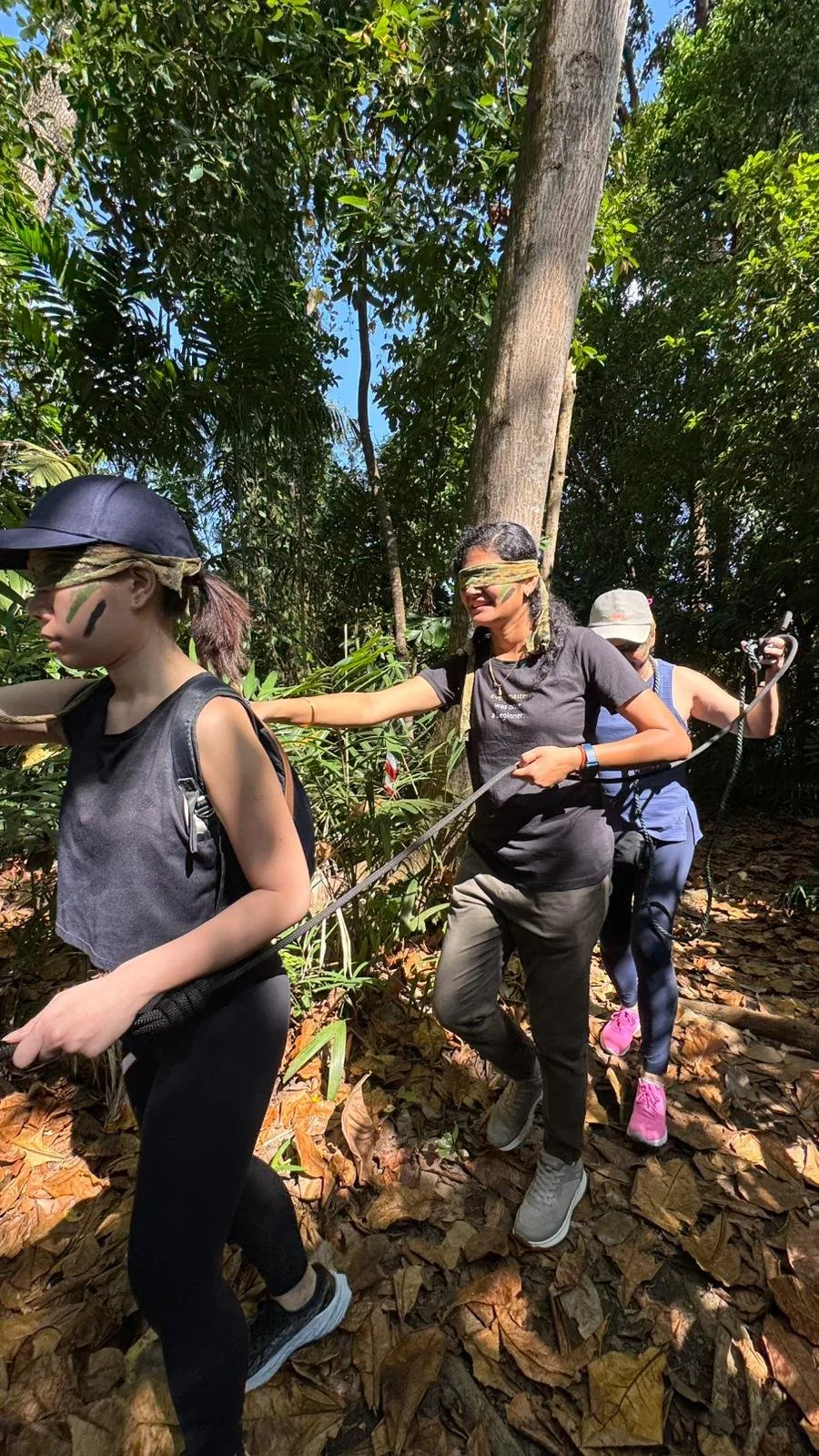 Team members with green face camouflage paint working through a rope challenge in the Fort Serapong jungle