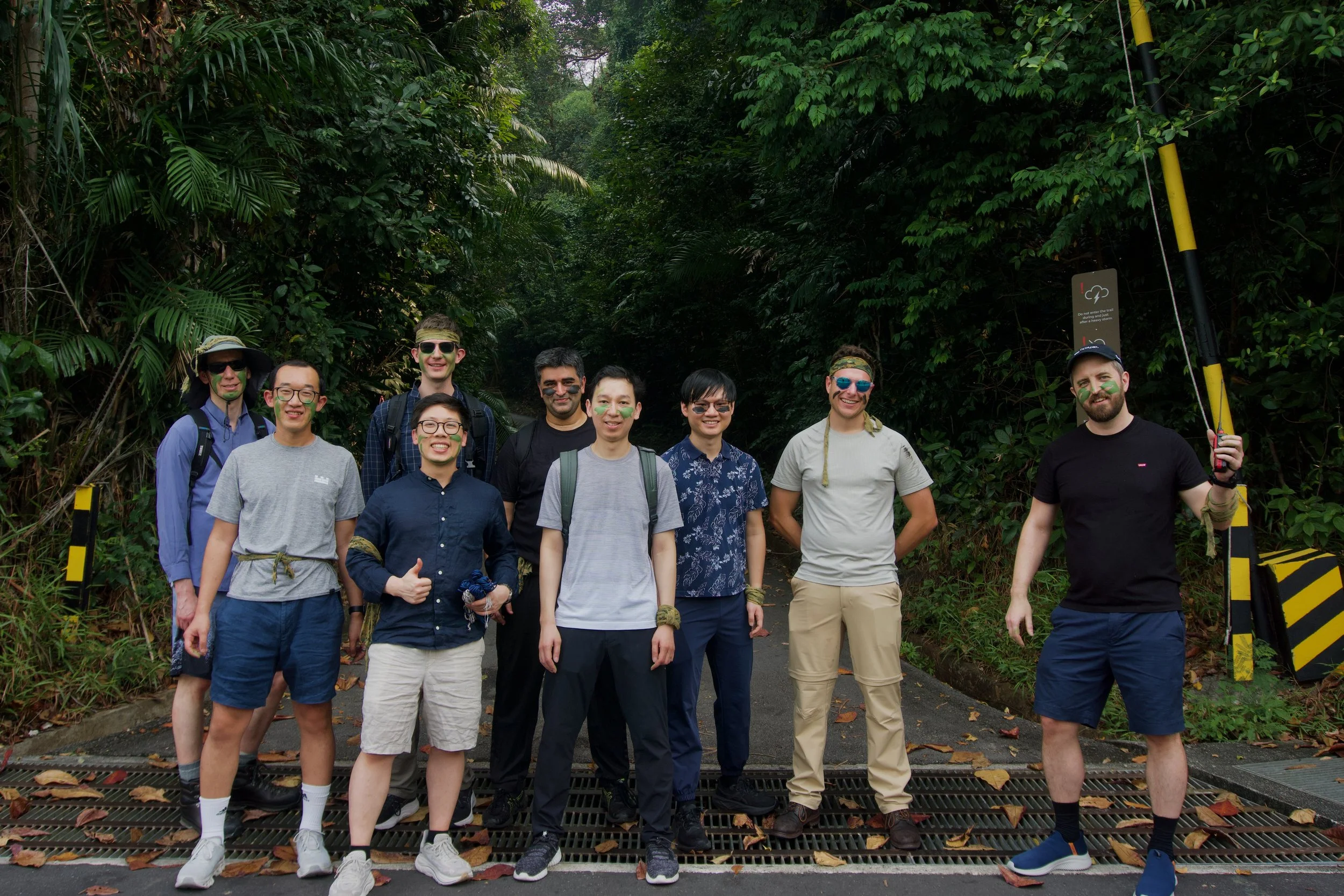 Nine Citadel Securities participants wearing camouflage face paint standing at the entrance road to Fort Serapong, Sentosa.