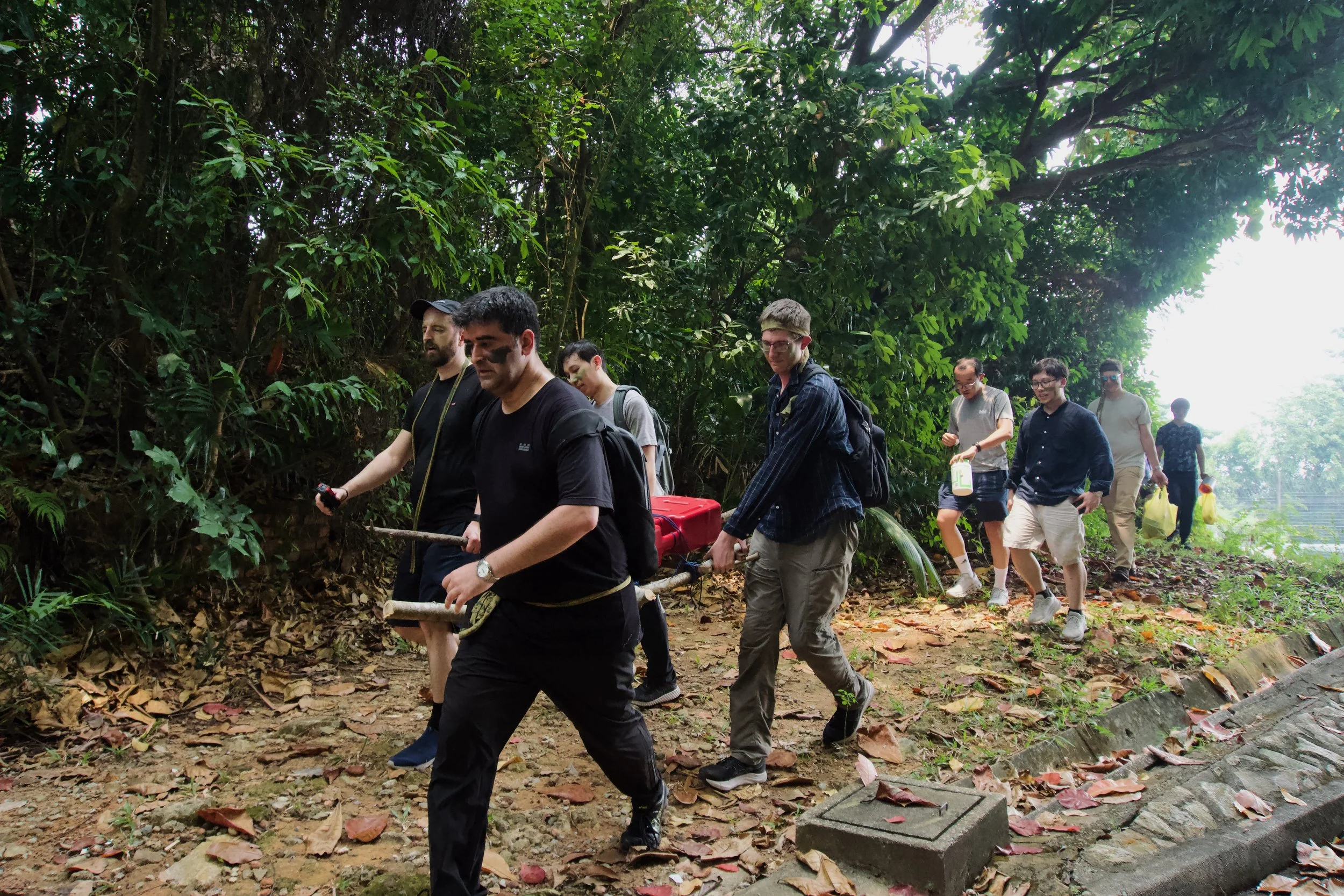 Citadel Securities team carrying a loaded improvised stretcher along a path through forest terrain at Fort Serapong.
