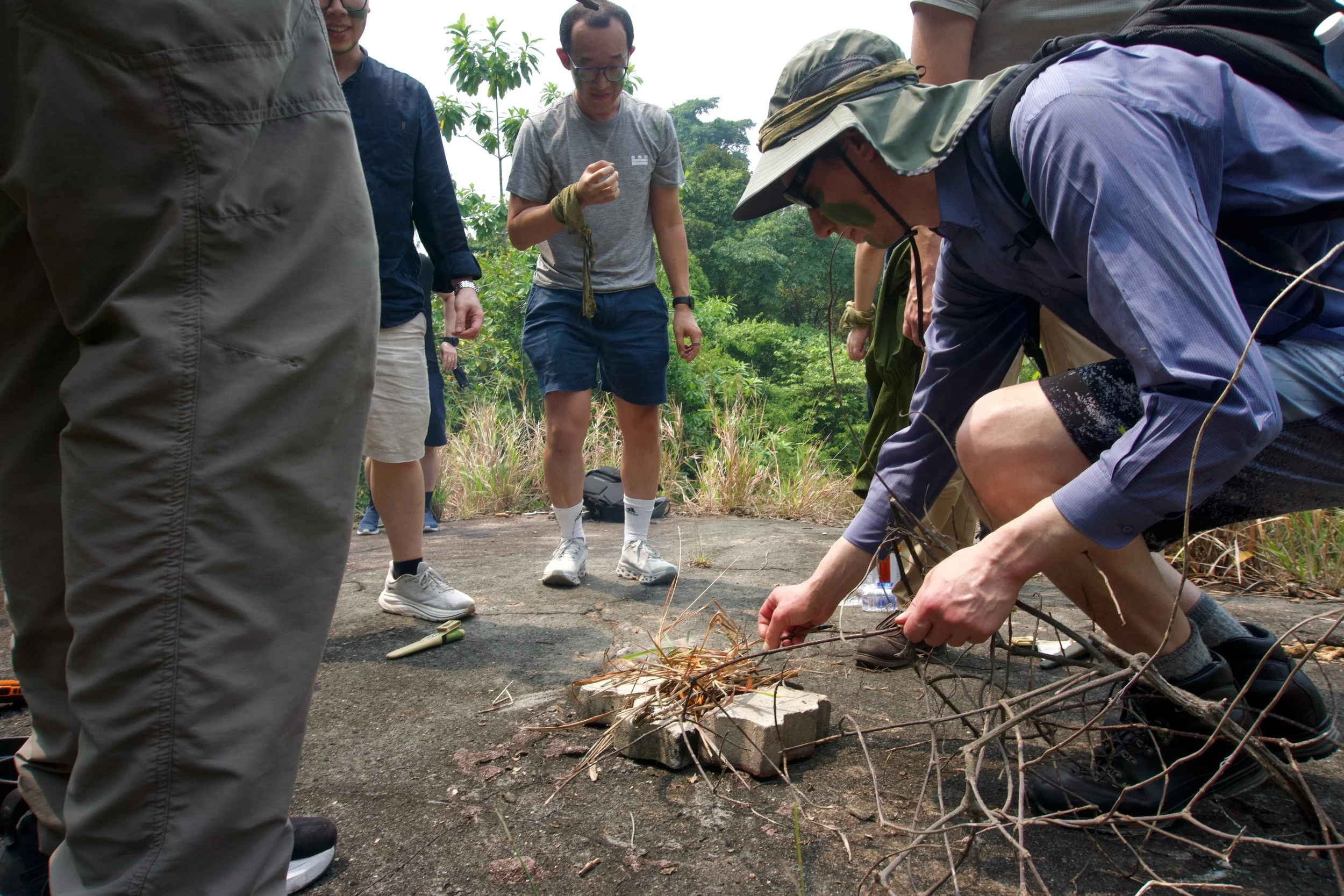 Citadel Securities participants preparing tinder and lighting a fire on open rock at Granite Hill, Fort Serapong.