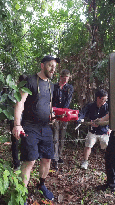 Citadel Securities participants loading a red 30-litre fuel can onto an improvised stretcher in forest terrain at Fort Serapong.