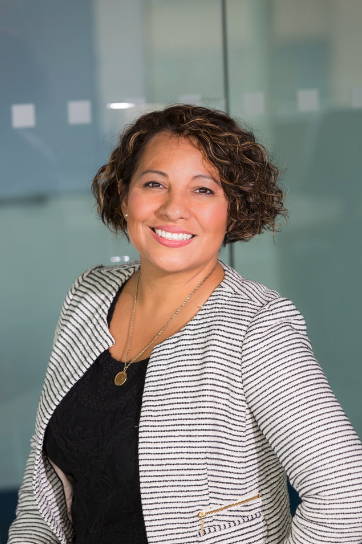 A woman smiling, wearing a black top and a striped blazer, in an office setting