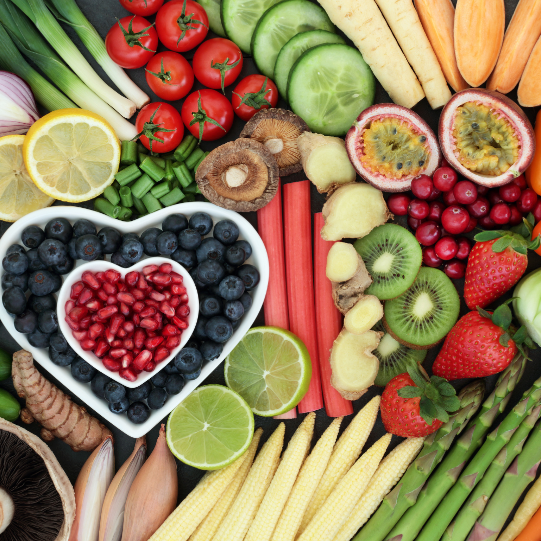 A colorful assortment of fresh fruits and vegetables including cherry tomatoes, cucumbers, passion fruit, strawberries, blueberries, pomegranate seeds, lemon, lime, baby corn, ginger, shiitake mushrooms, kiwi, rhubarb, and various root vegetables.