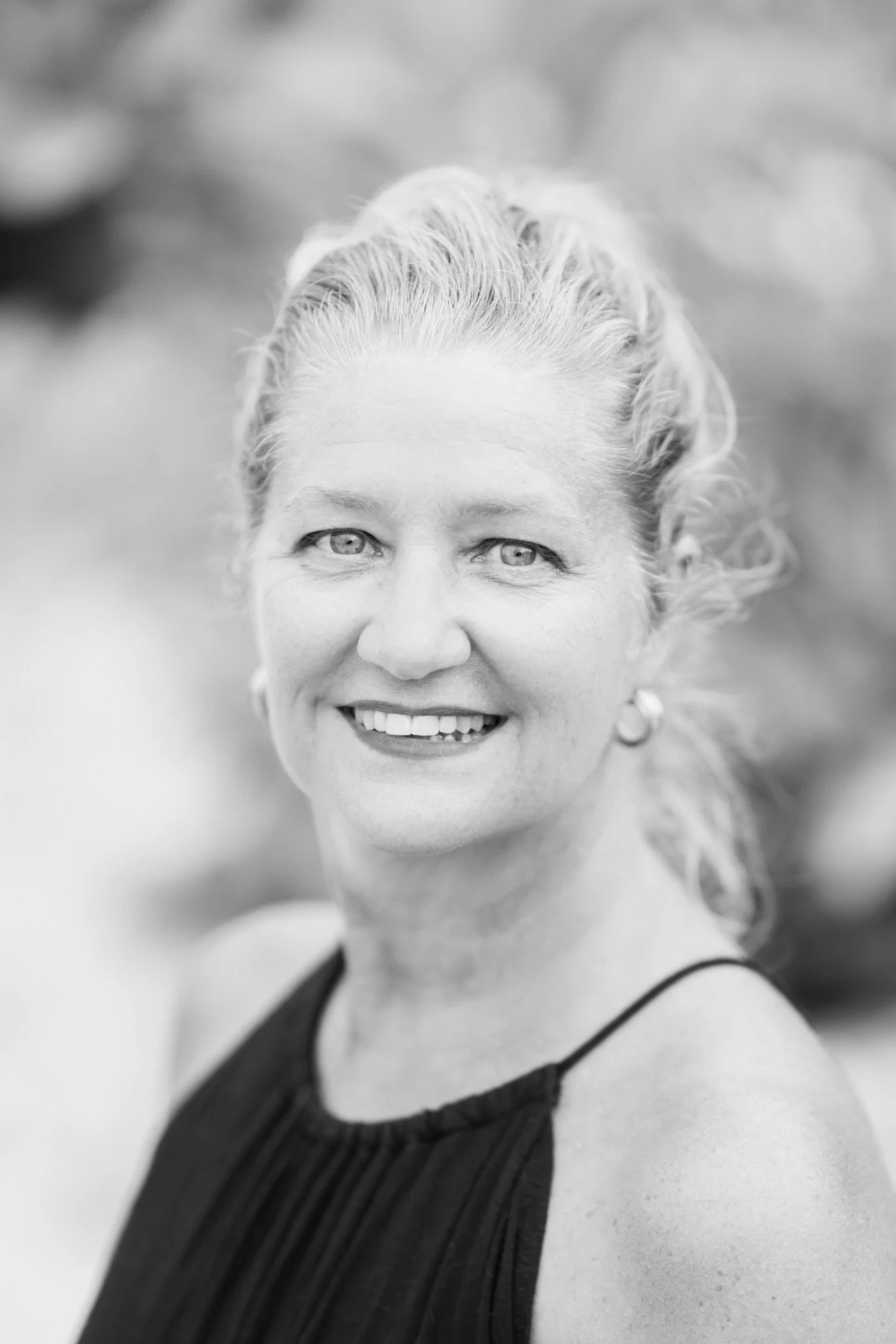 Black and white portrait of a smiling woman with wavy hair, earrings, and a sleeveless top.