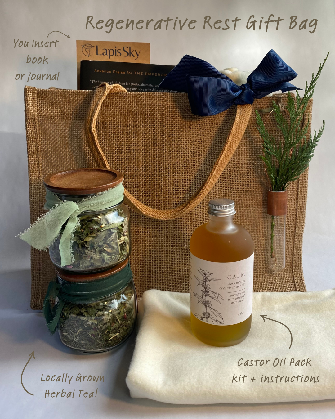 A gift bag labeled 'Regenerative Rest Gift Bag' containing a book or journal, a sprig of greenery in a test tube, two jars of locally grown herbal tea with cloth ribbons, and a castor oil pack kit with instructions placed on a cream cloth.