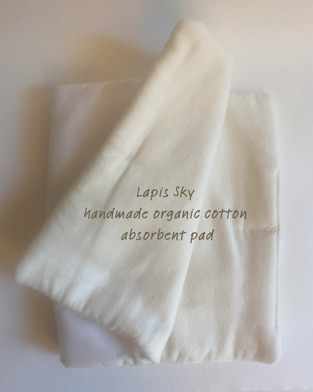 A folded white cotton absorbent pad with text overlay that reads 'Lapis Sky, handmade organic cotton absorbent pad'.