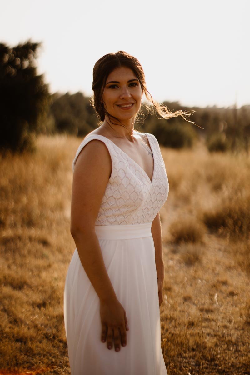 Une femme en robe blanche dans un champ au coucher du soleil.