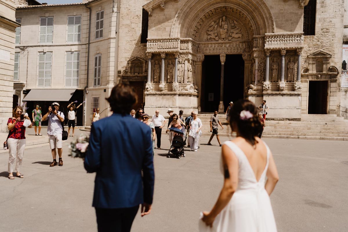 Un couple de mariés marche vers une église avec des invités prenant des photos devant le bâtiment.