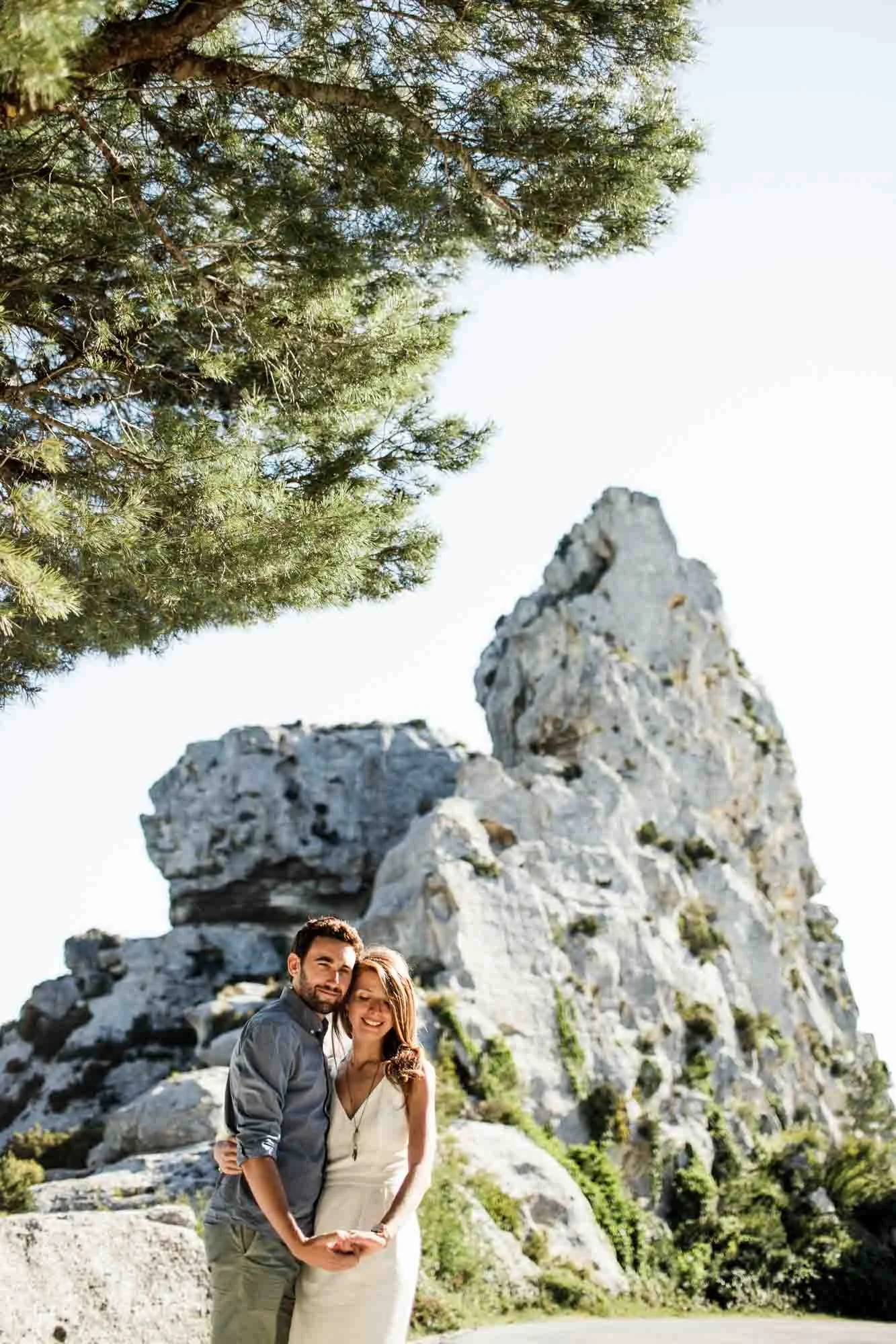 Un couple souriant devant des formations rocheuses et un arbre.