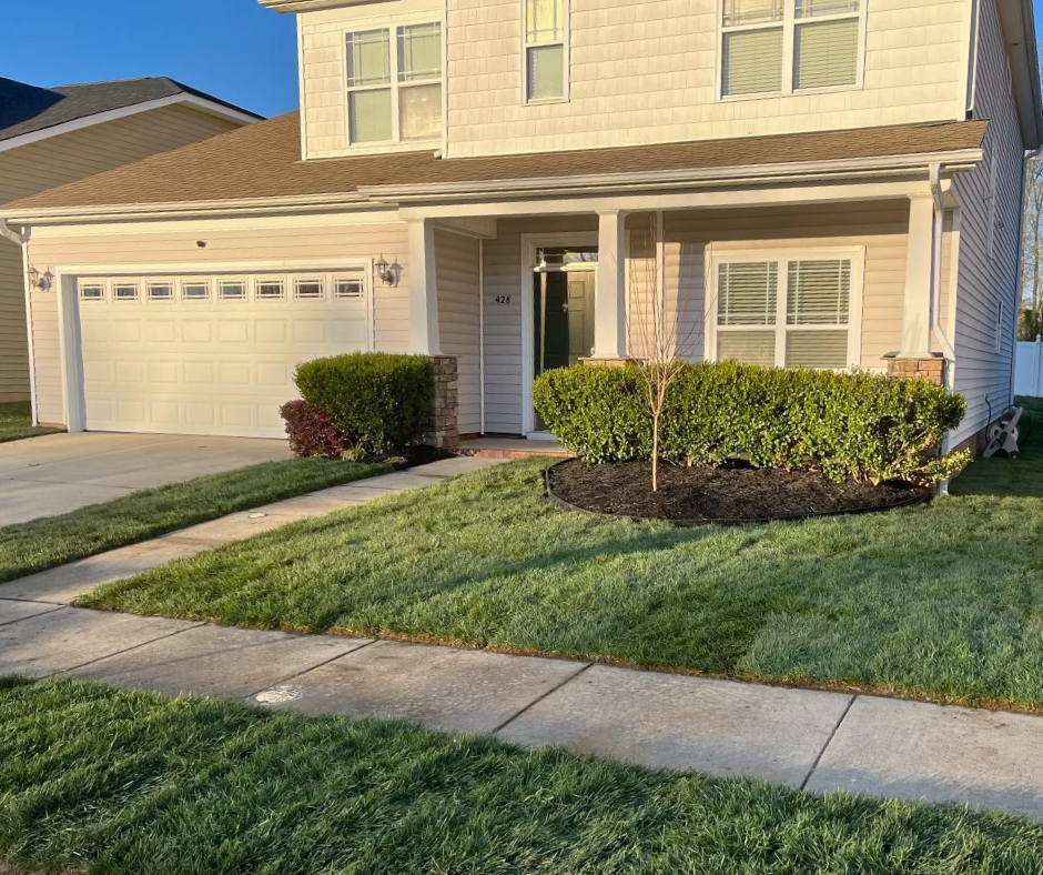 After photo of a refreshed front yard with newly installed sod, trimmed shrubs, and a clean mulched bed in front of a two-story home
