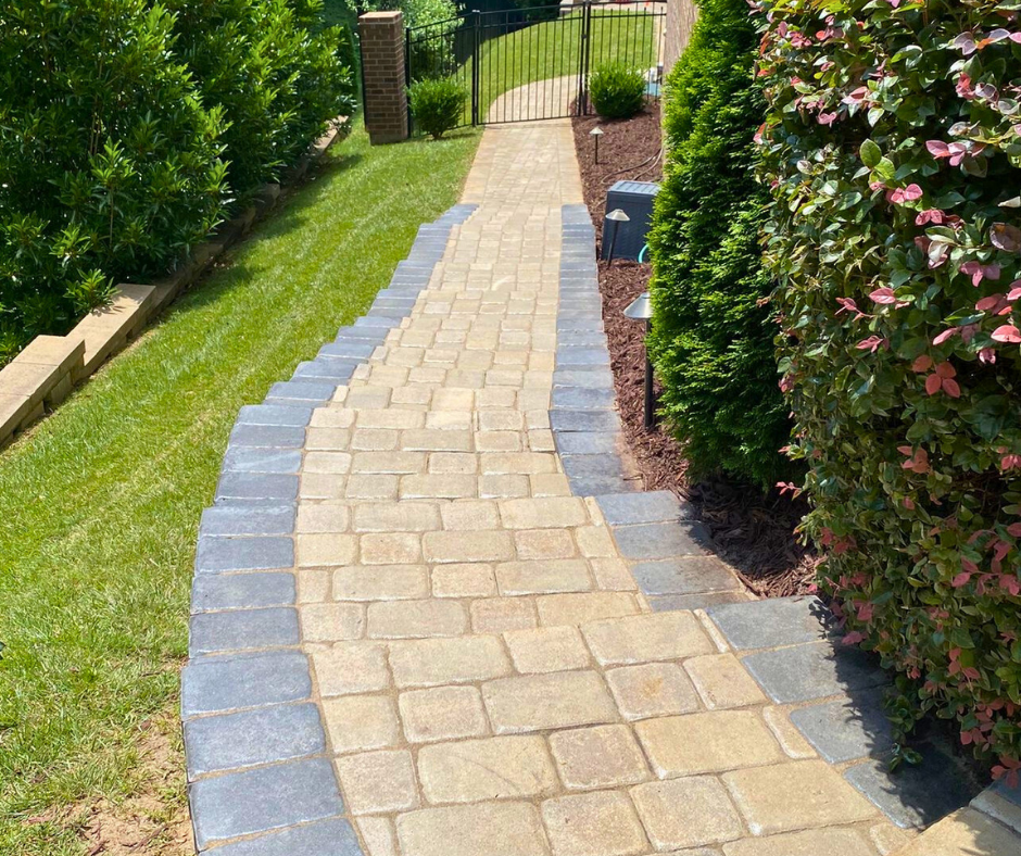 Curved stone paver stairway bordered with darker edge pavers, leading through a landscaped yard toward a metal gate