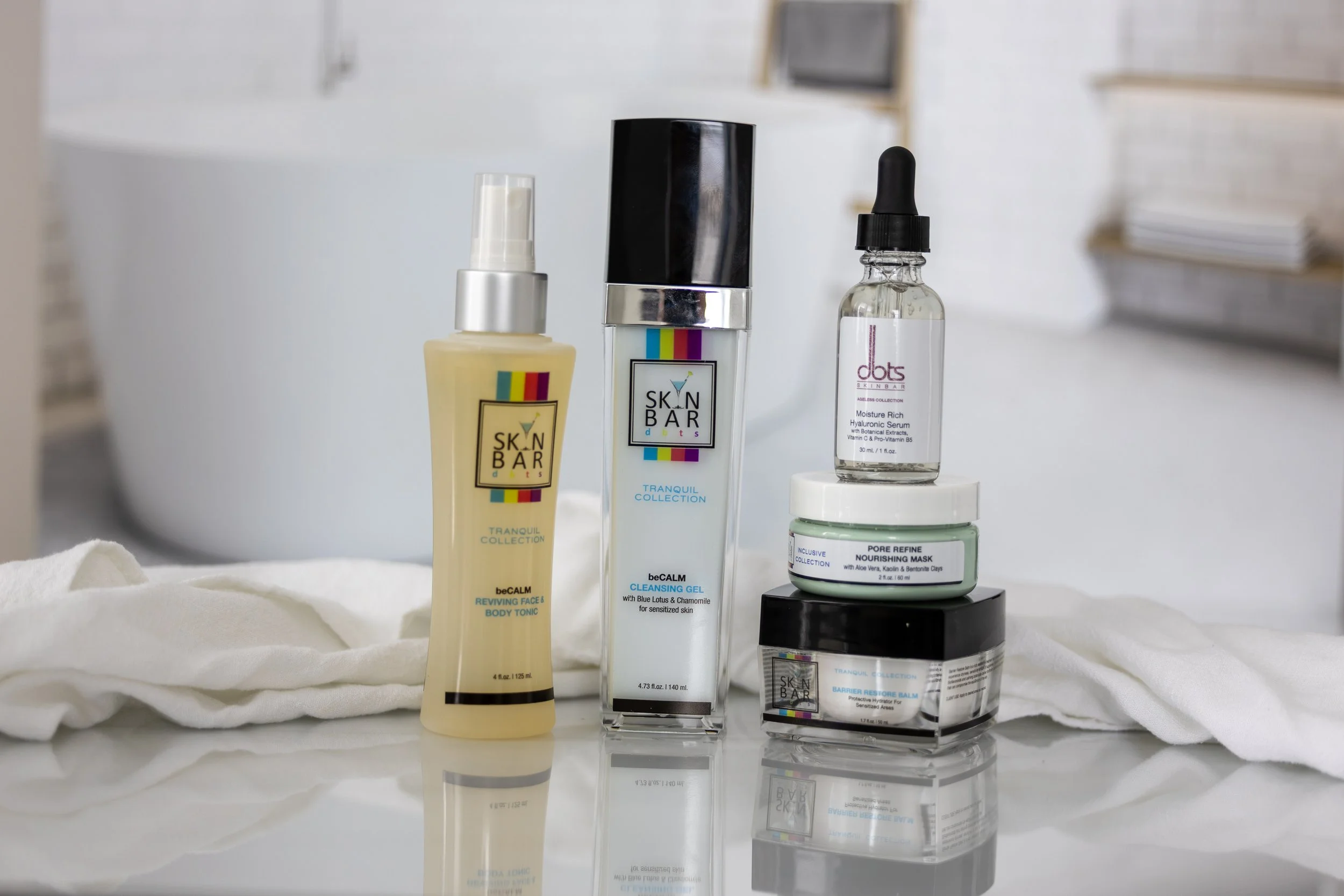 Skincare products arranged on a white surface, including sprays, gels, creams, and serums, with a white towel in the background.