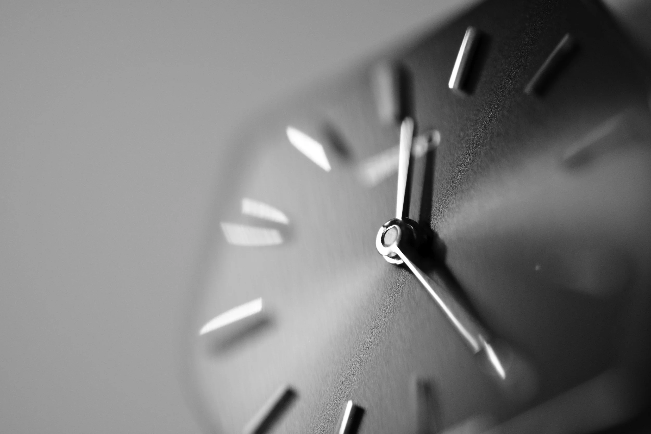 Close-up of a clock face, showing silver hands and hour markers with light reflections and shadows.
