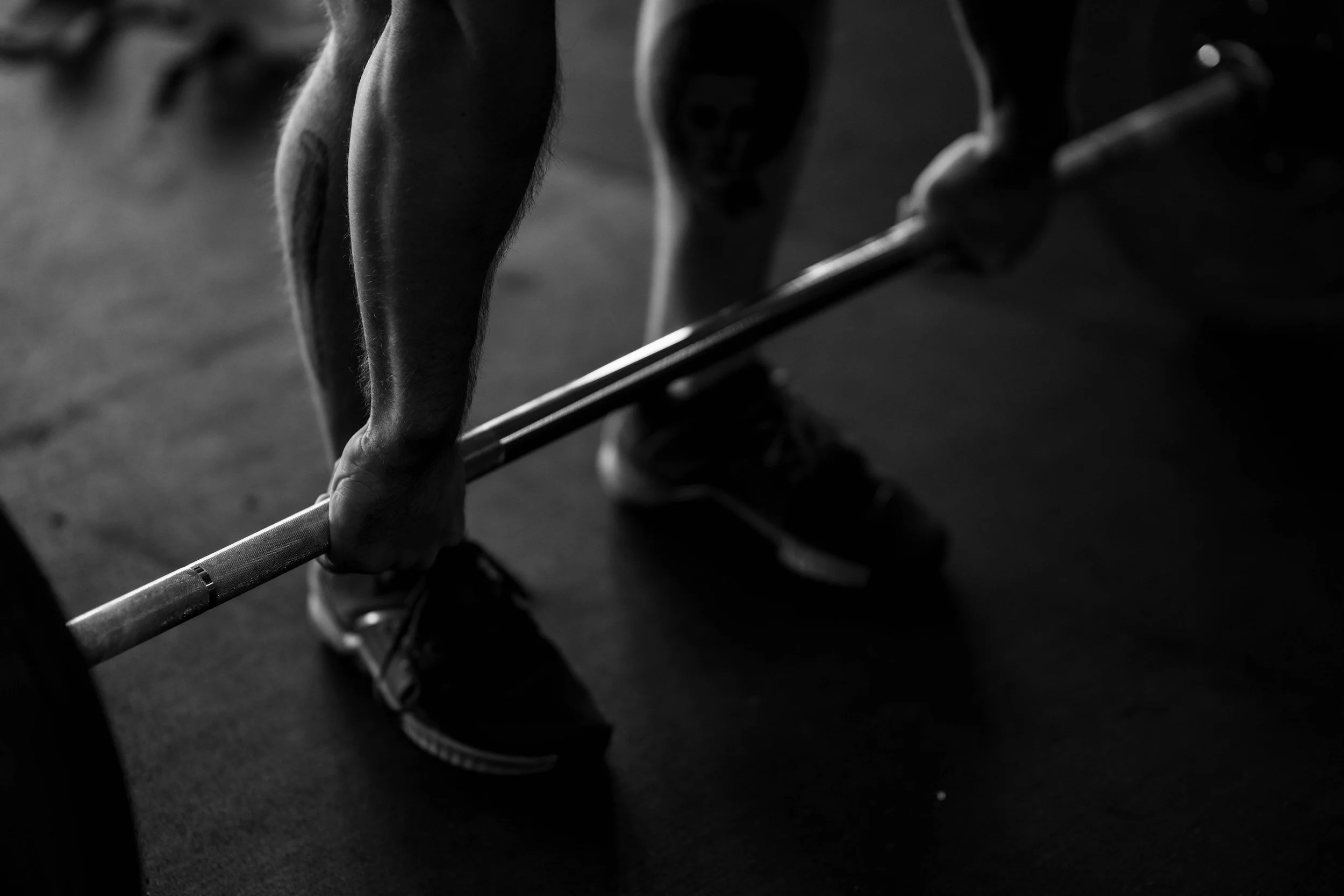 A person is preparing to lift a barbell during a workout in a gym, with a focus on their hands and legs in black and white.