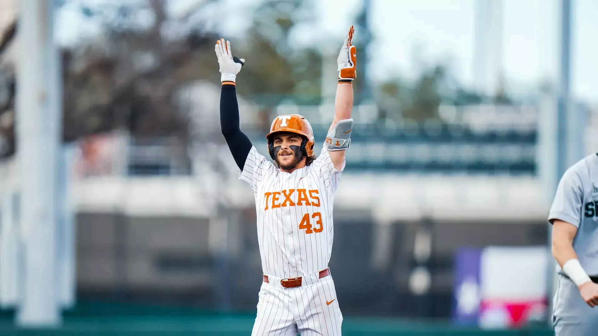 Aiden Robbins throws both hands up in the air celebrating his hit. He's wearing a pinstripe Texas uniform with the number 43