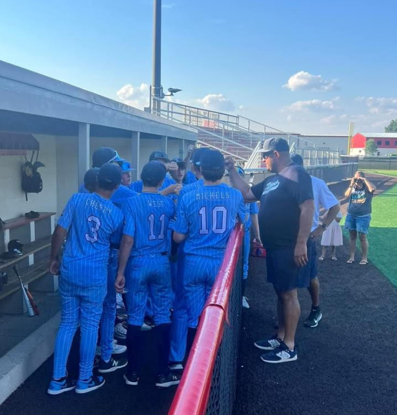 A team of middle-school aged baseball players in a huddle in the dugout. They are wearing light blue pinstripe jerseys.