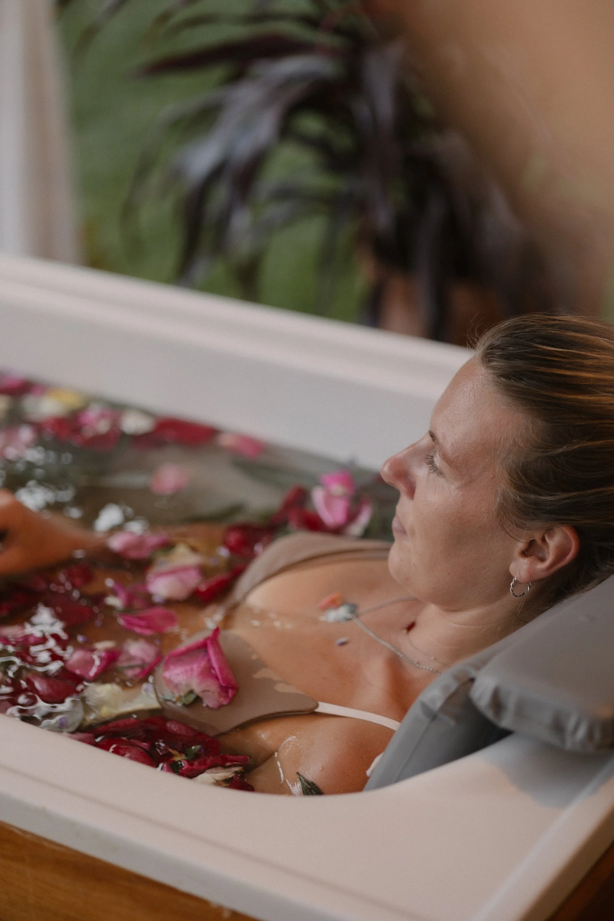 Mujer disfrutando de un baño de spa con pétalos de rosa en una tina.