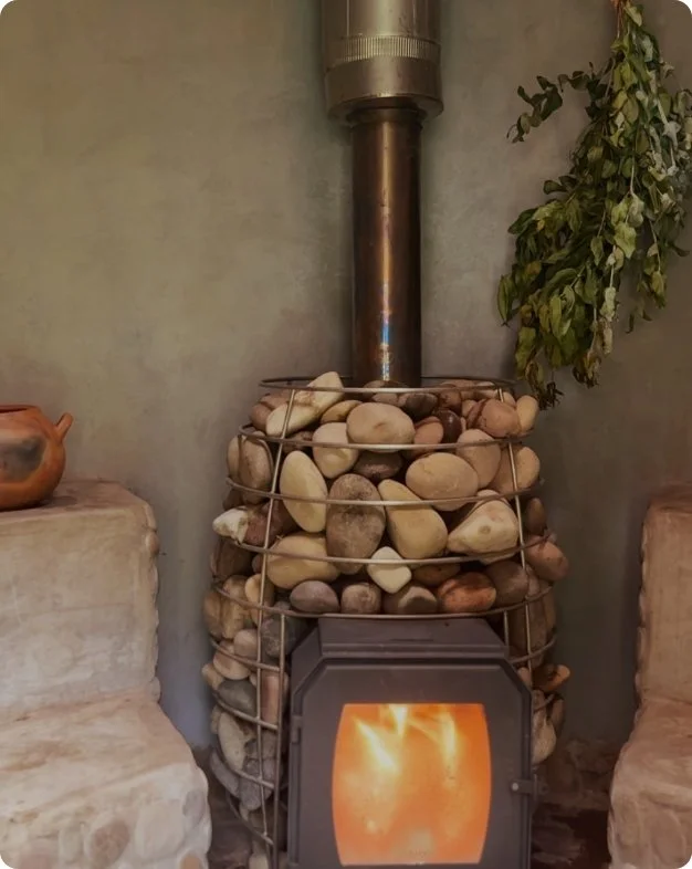 Estufa de leña con una estructura de piedra y una rejilla de metal, en encendido, en una esquina de una habitación con paredes de color gris, decorada con plantas.