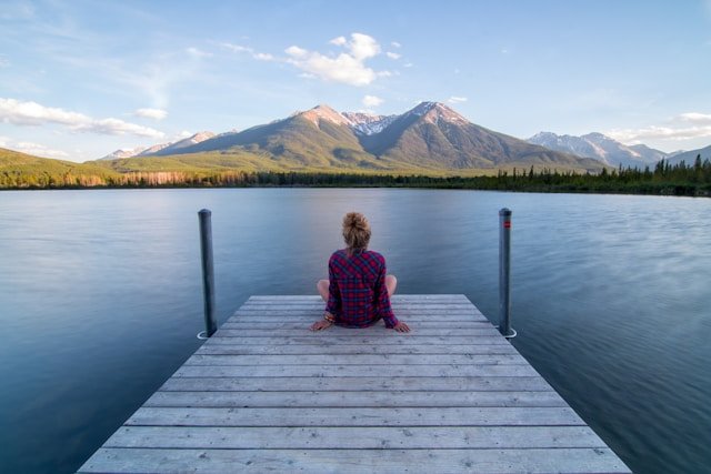 Person sitting on a dock overlooking a mountain lake, reflecting on emotional suppression and emotional healing.