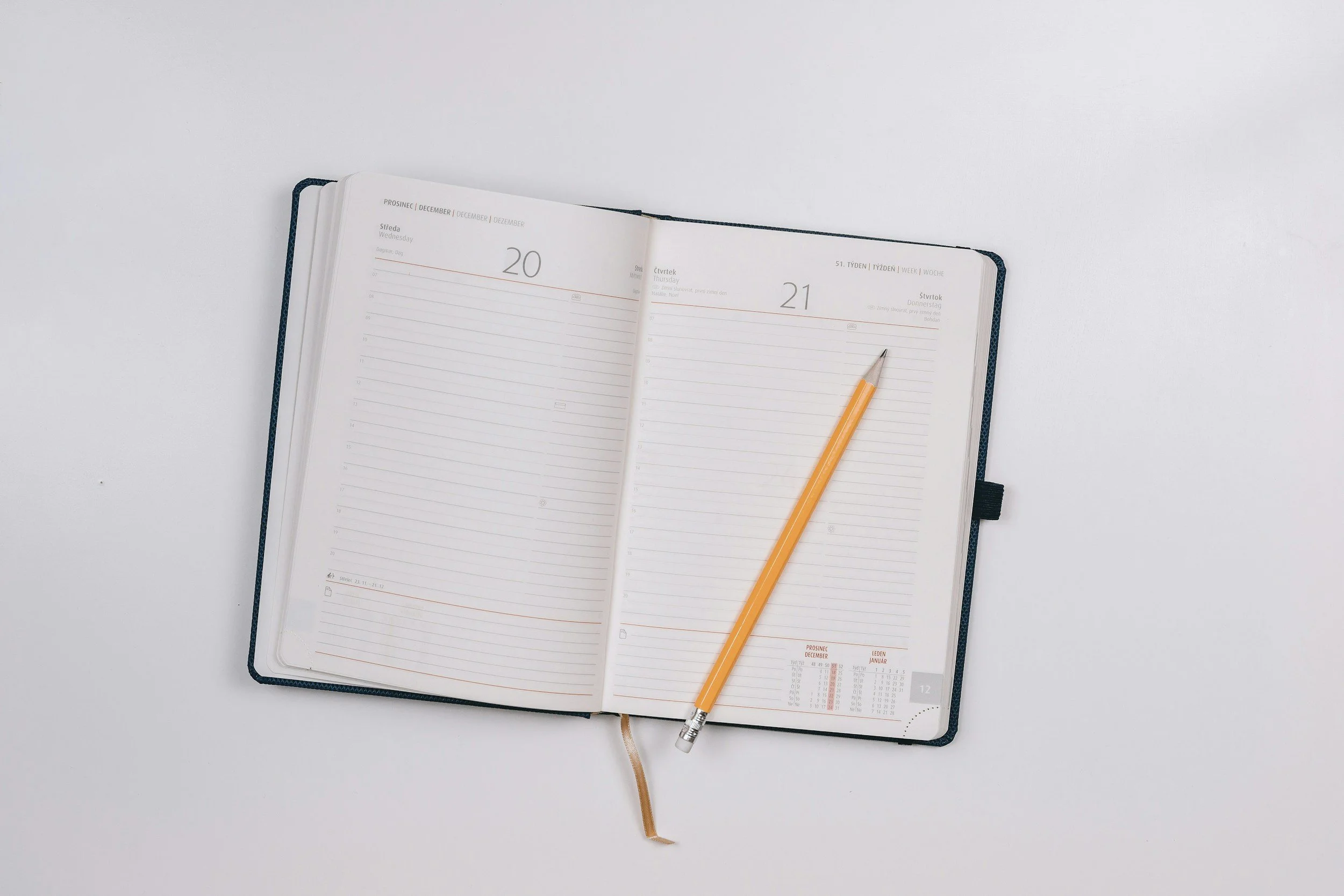 Open planner or diary with a yellow pencil laying on the right page, showing the dates 20 and 21, on a white surface.