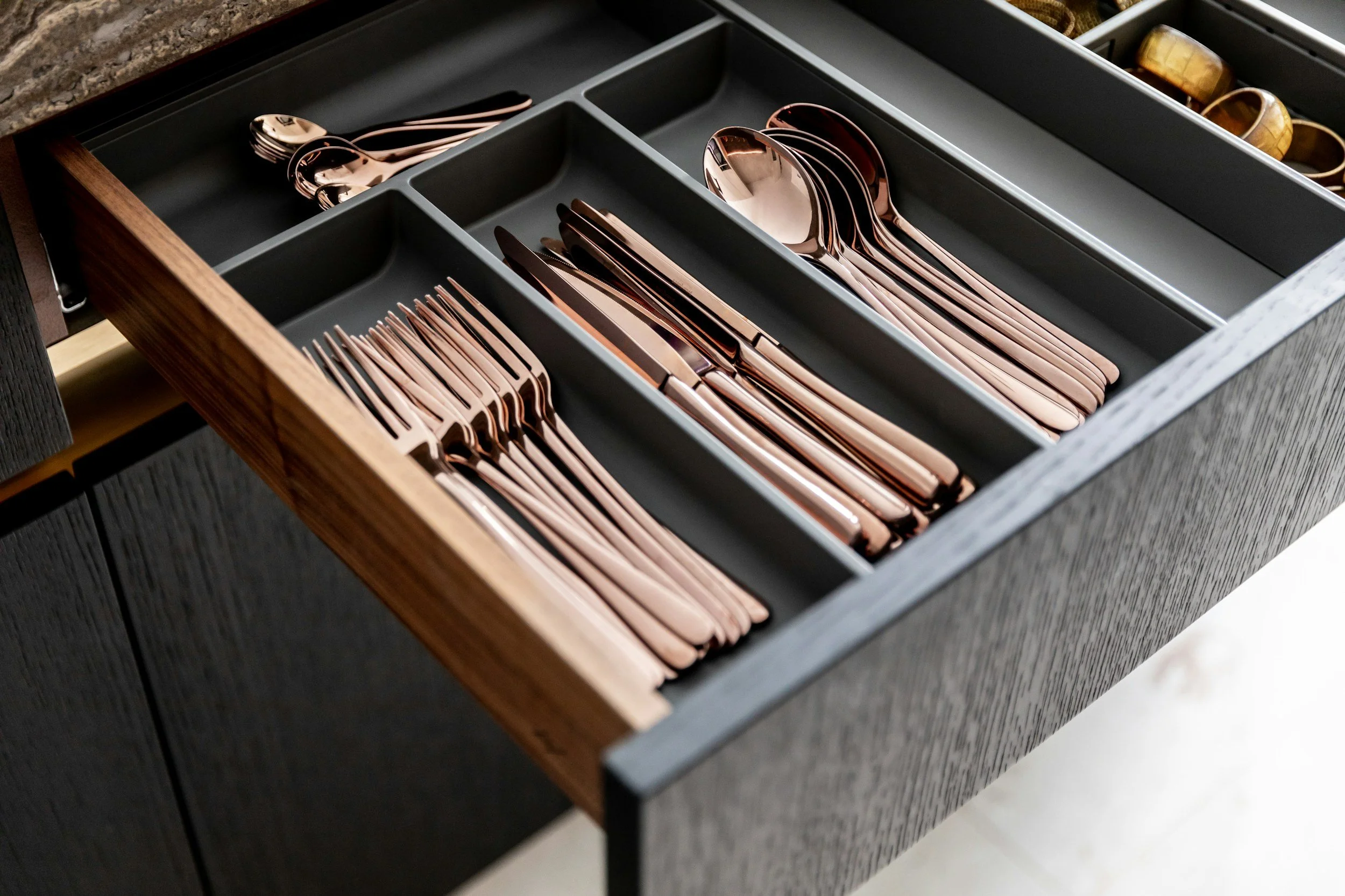 Drawer with organized rose gold cutlery, including forks, knives, and spoons, in separate compartments.
