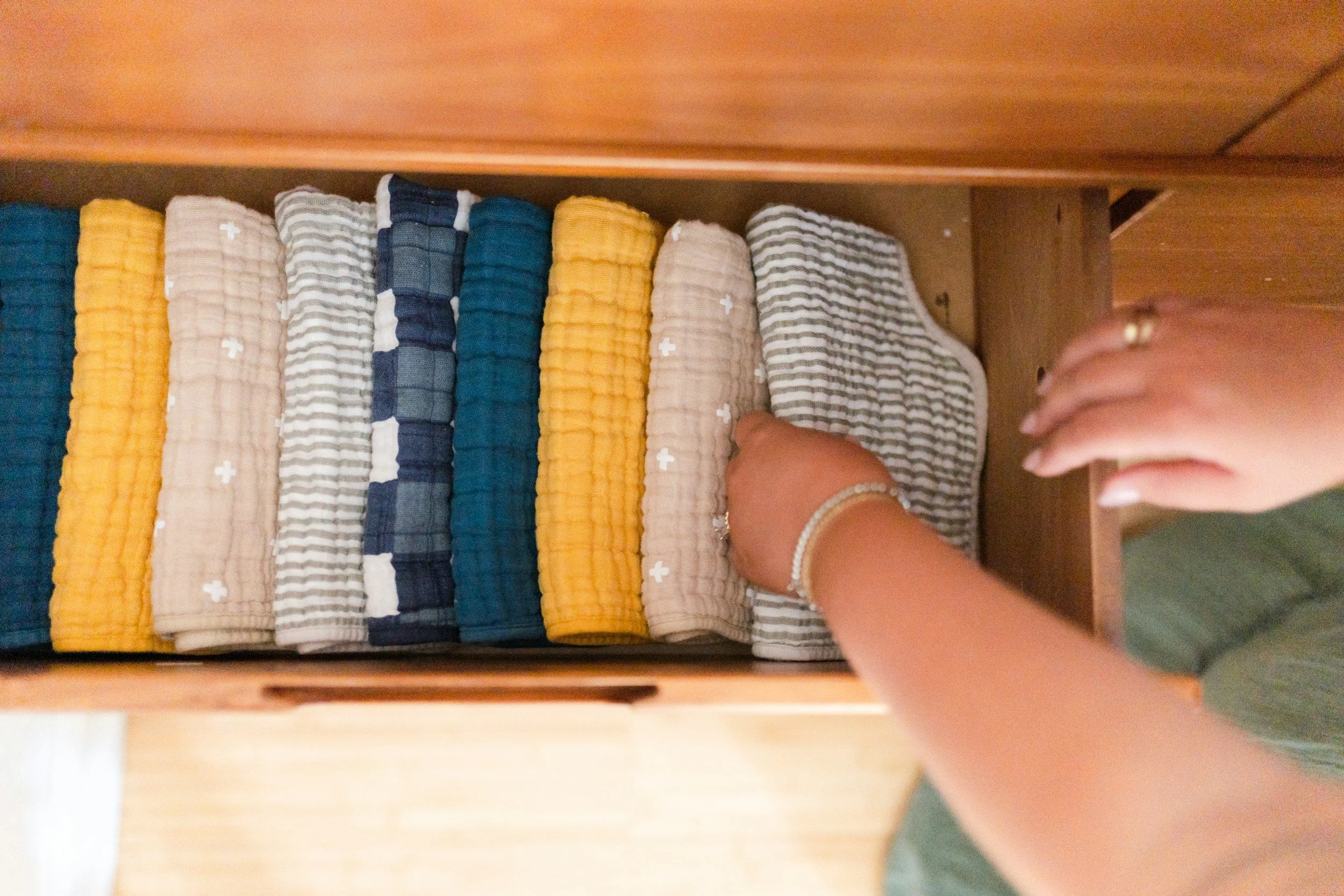 A person organizing multicolored cloth diapers in a wooden drawer.