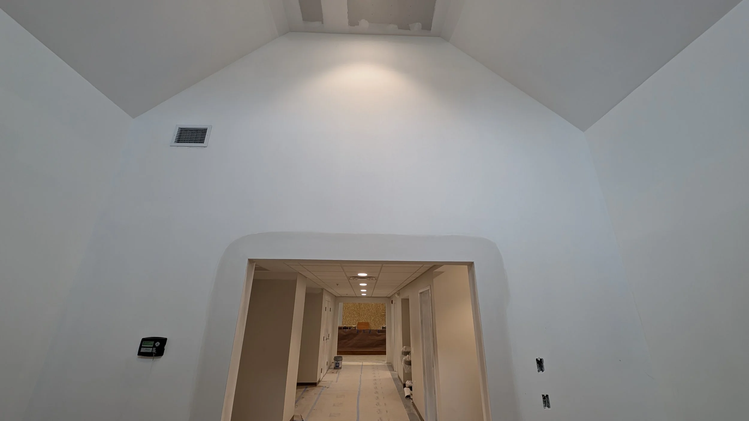 Interior of a room under construction with a high vaulted ceiling, white walls, and recessed lighting.