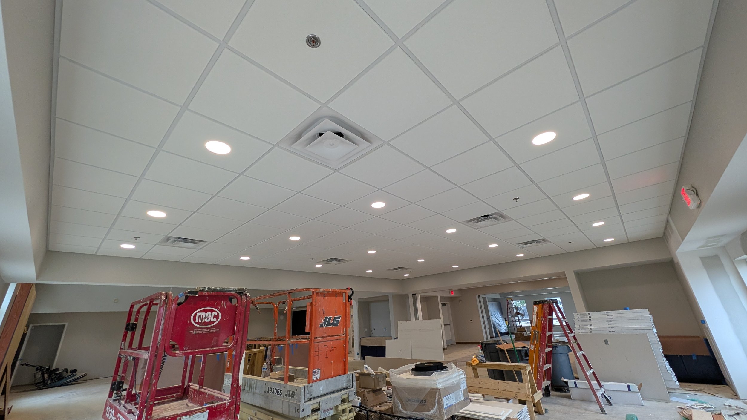 Construction site with ceiling lights, some construction equipment, and building materials in an unfinished room.