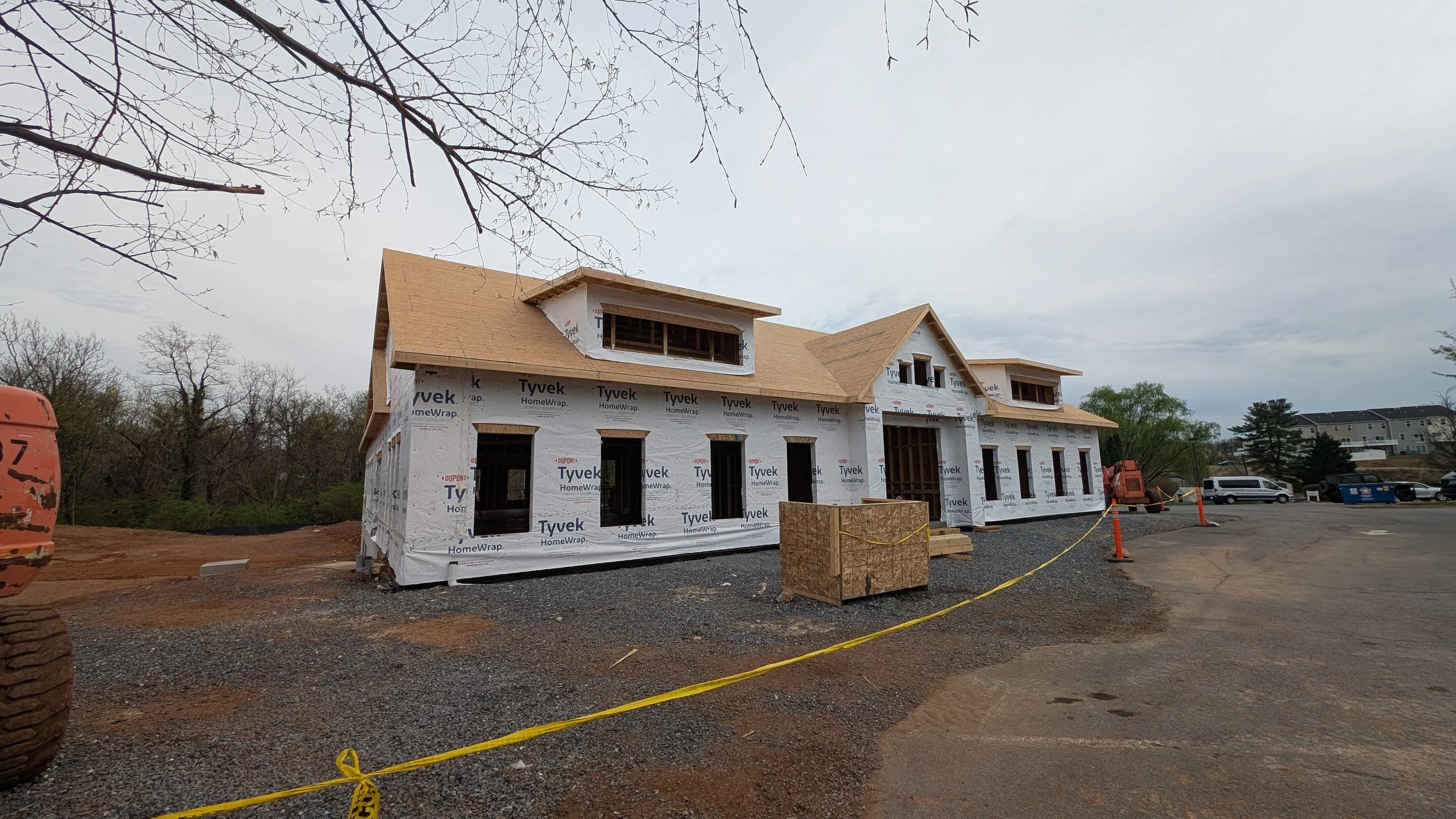 A house under construction with unfinished walls and roof, surrounded by construction equipment and orange safety cones.