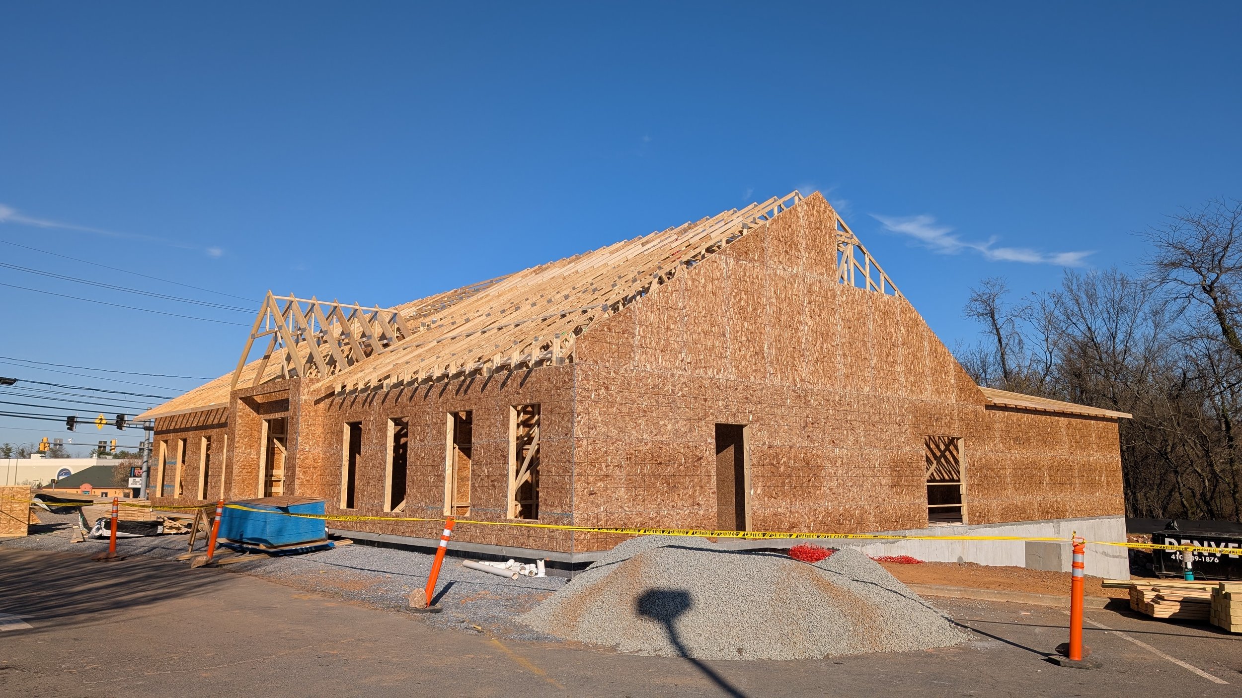 Construction site of a wooden building frame with plywood walls and roof trusses under a clear blue sky.