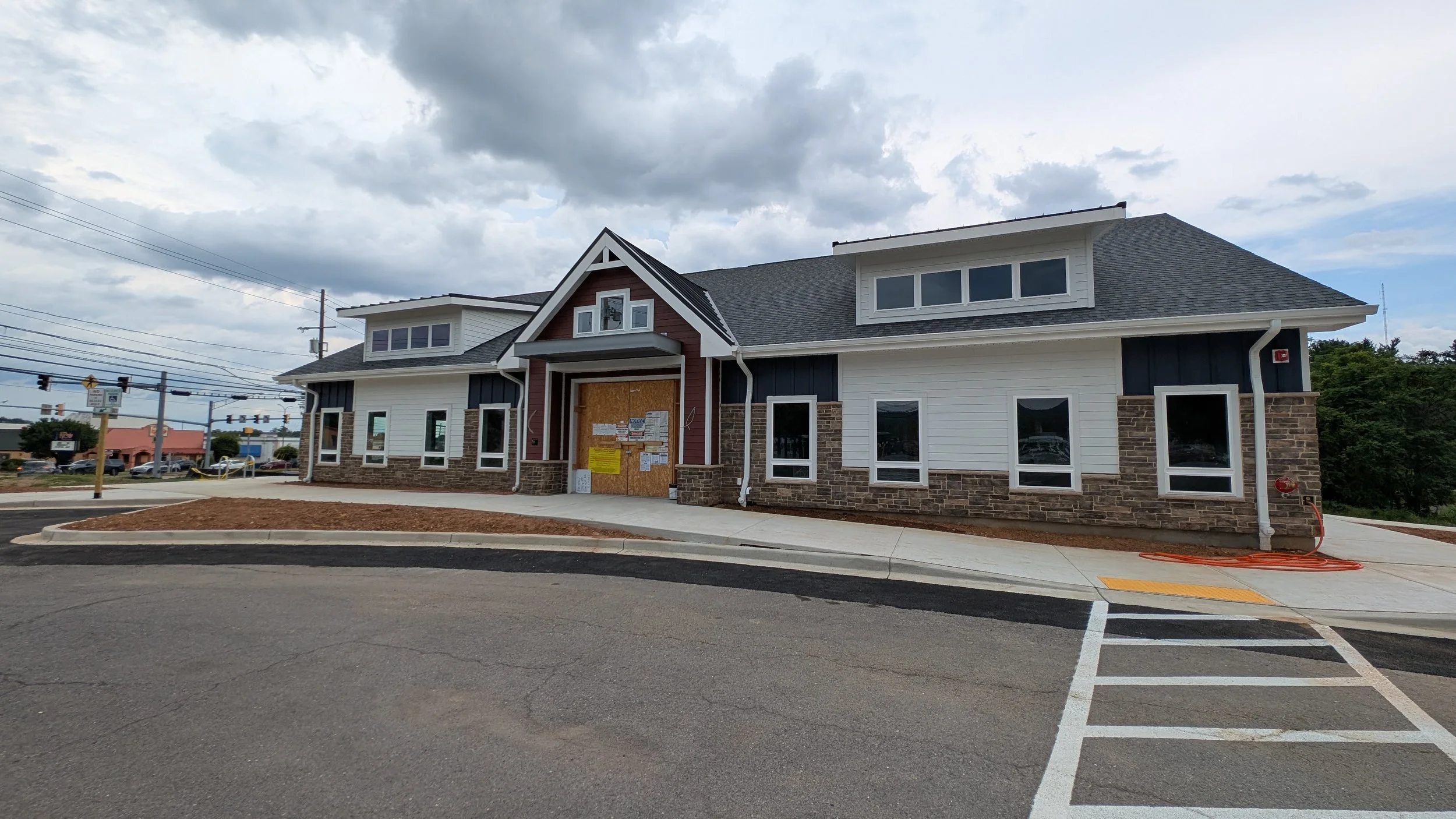 A new commercial building under construction with boarded-up entry, surrounded by a parking lot and street, partly cloudy sky overhead.