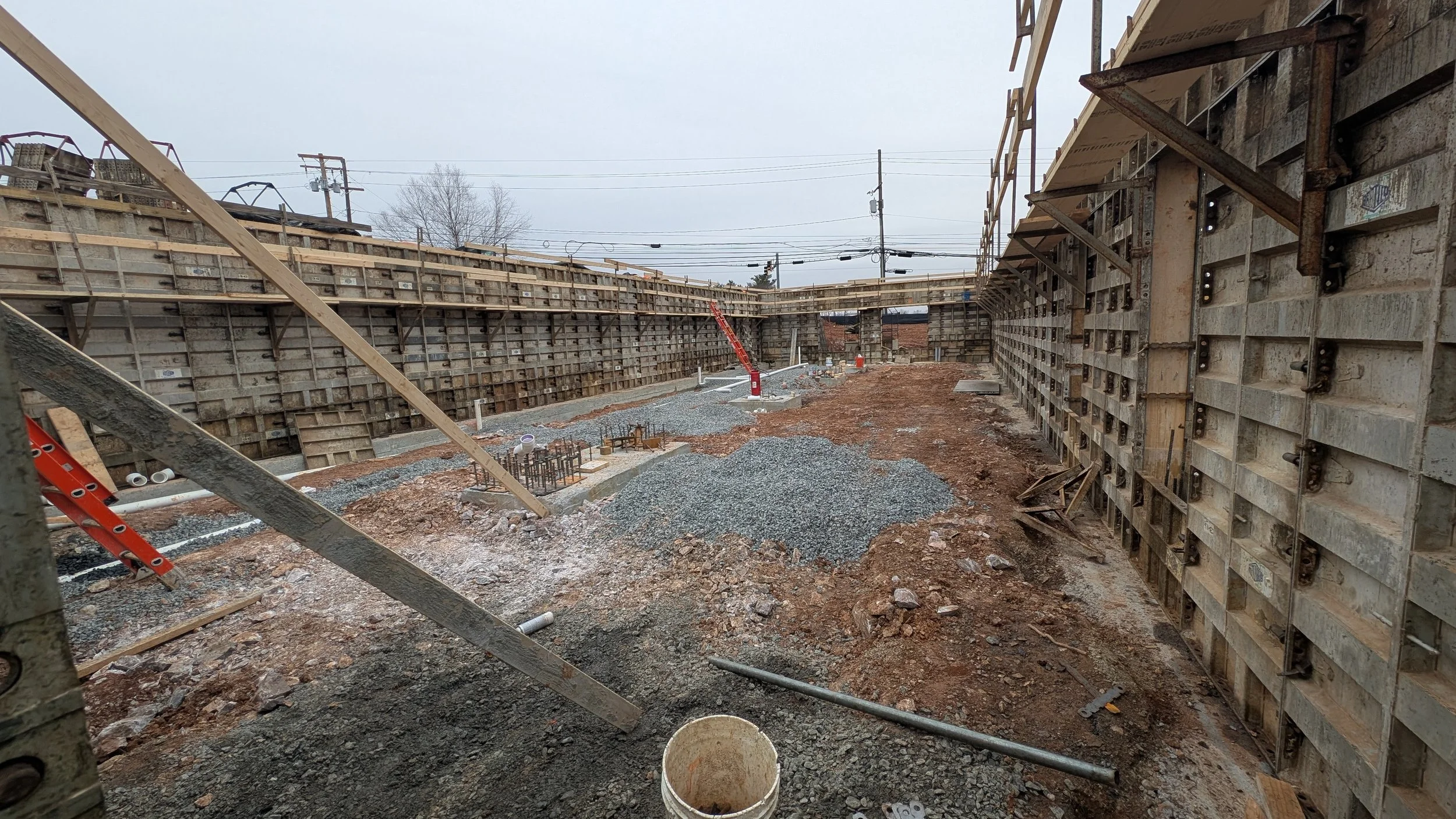 Construction site with deep excavation, retaining walls, scaffolding, and construction equipment.