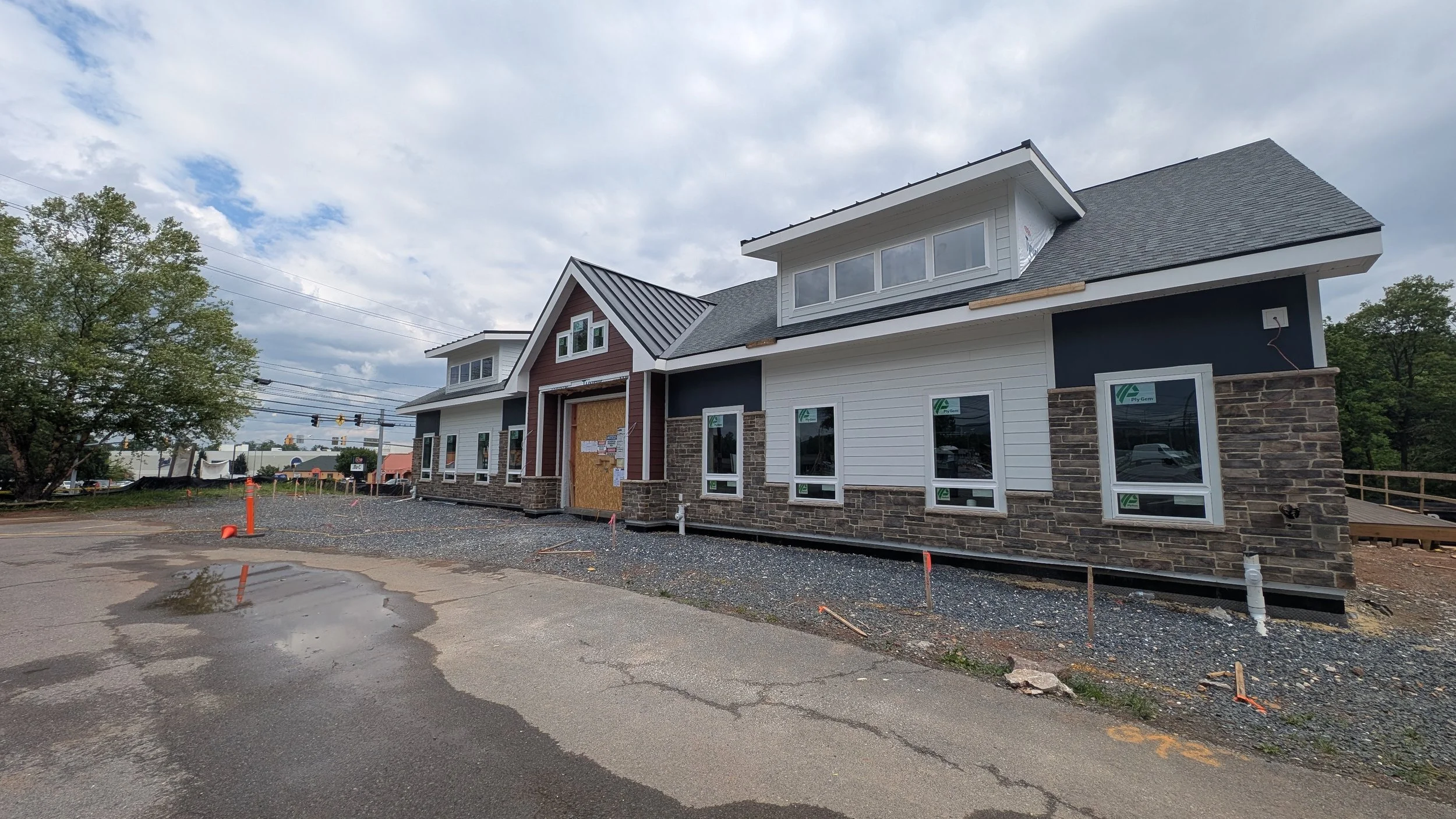 Under construction building with siding and stone facade, multiple windows, and a boarded-up doorway, on a cloudy day.