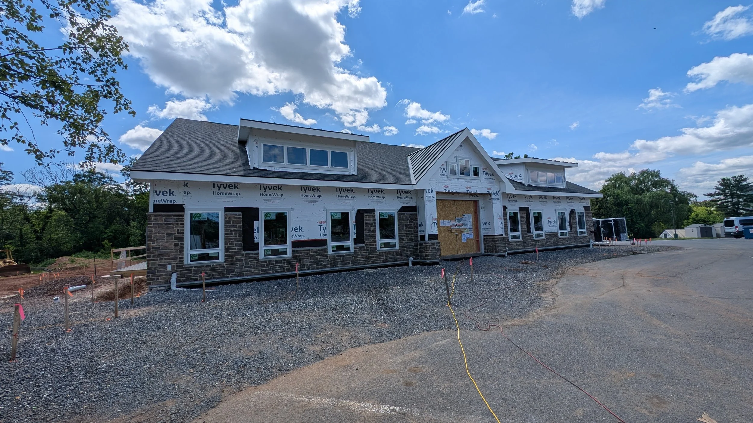 Under construction house with a stone exterior, multiple windows, and a gray roof under a partly cloudy sky