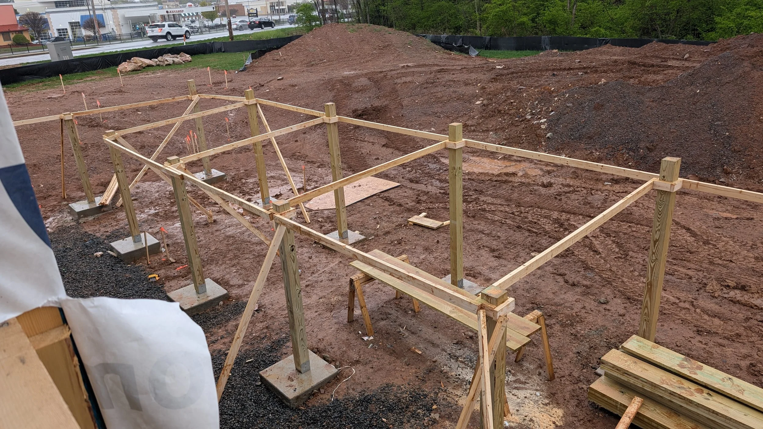 A construction site with a frame of wooden supports and stakes, and a pile of dirt in the background.
