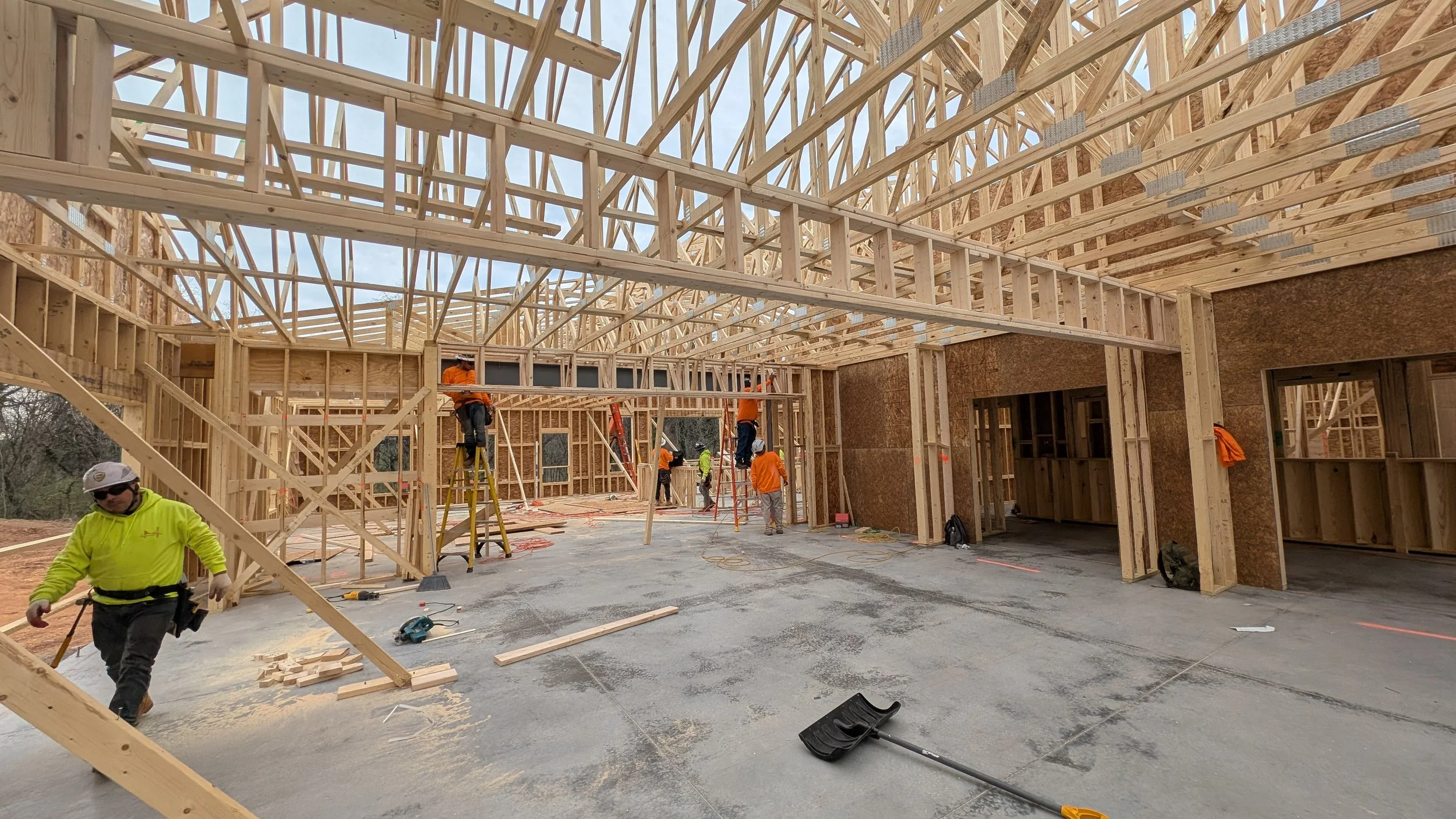 Construction workers installing wooden framing and roof trusses inside a building under construction.