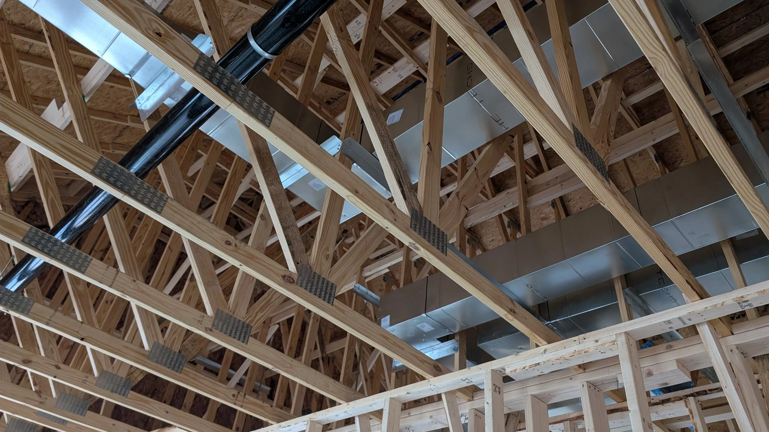 Construction framing with exposed wooden beams and ceiling ductwork inside a building under construction.