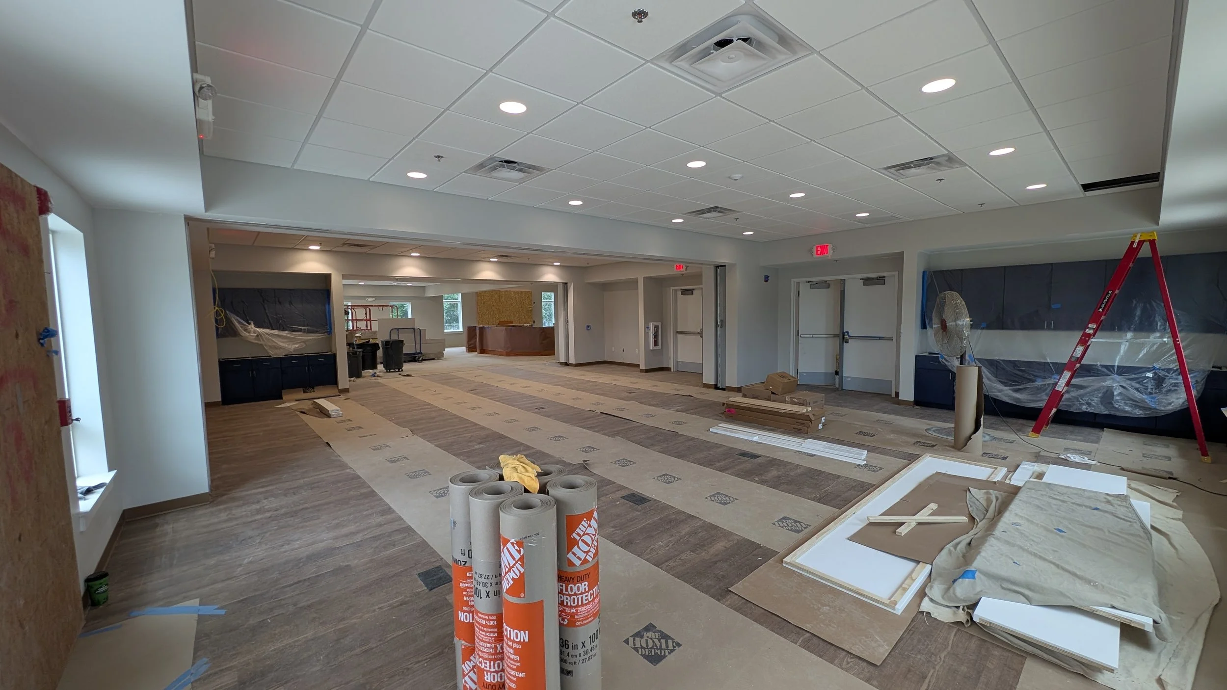 Interior of a building under renovation with construction materials, ladders, and protective coverings on the floor and walls.