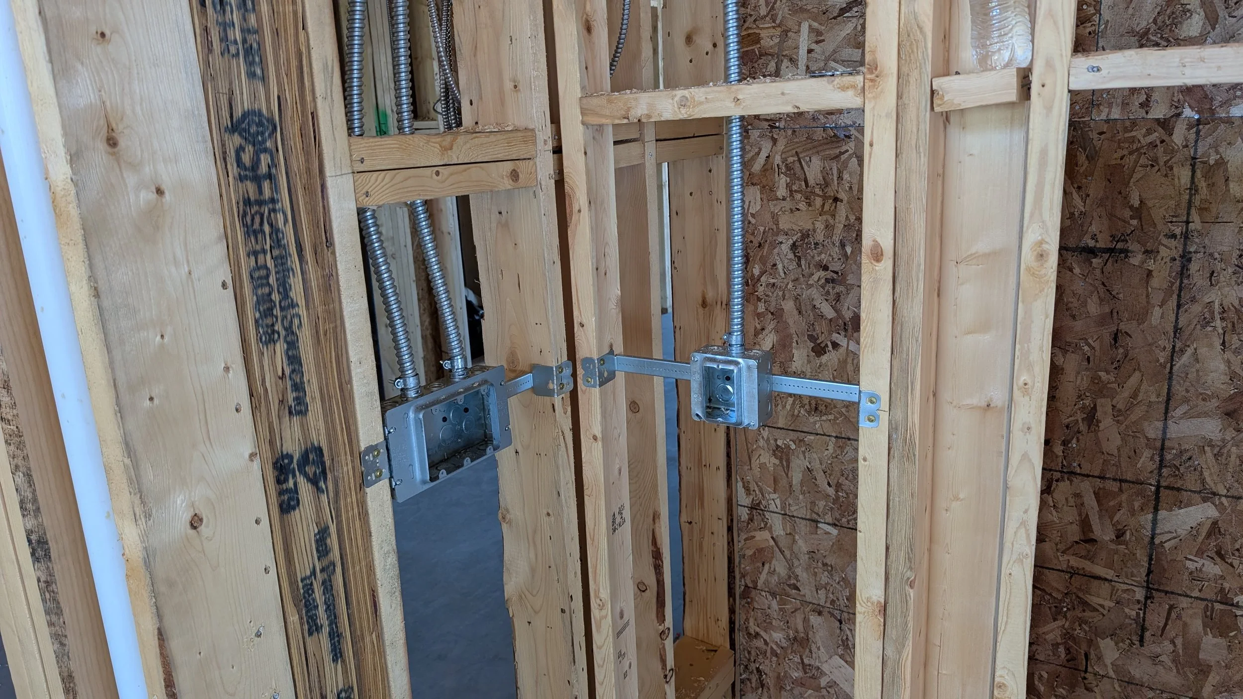 Electrical wiring and metal electrical boxes installed in a wooden wall frame under construction.