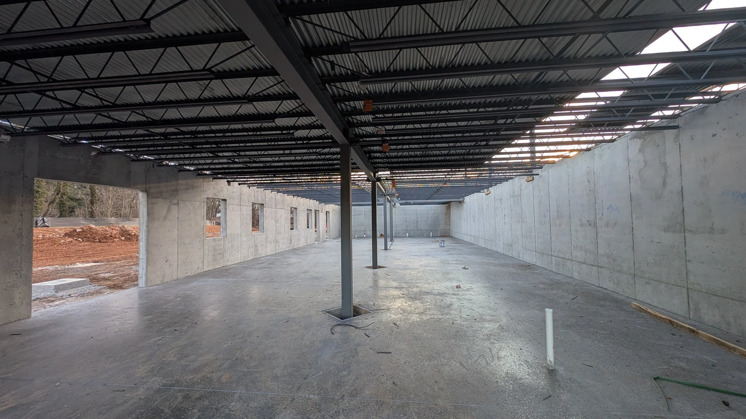 Construction site with concrete walls and steel support beams, open windows, and an unfinished ceiling with exposed insulation and roofing materials.