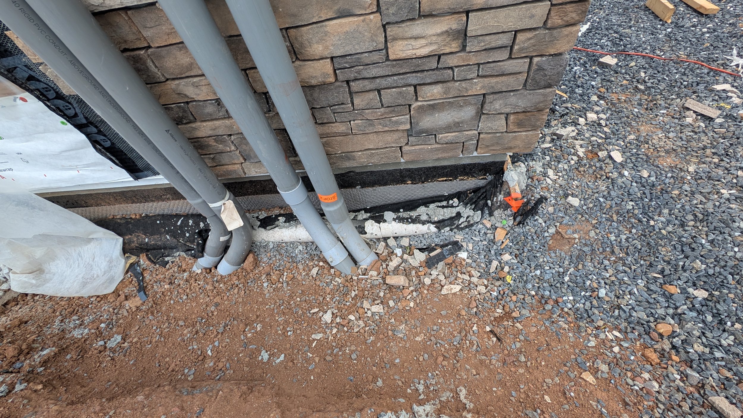 Installation of exterior pipes next to a brick wall with insulation and gravel ground.