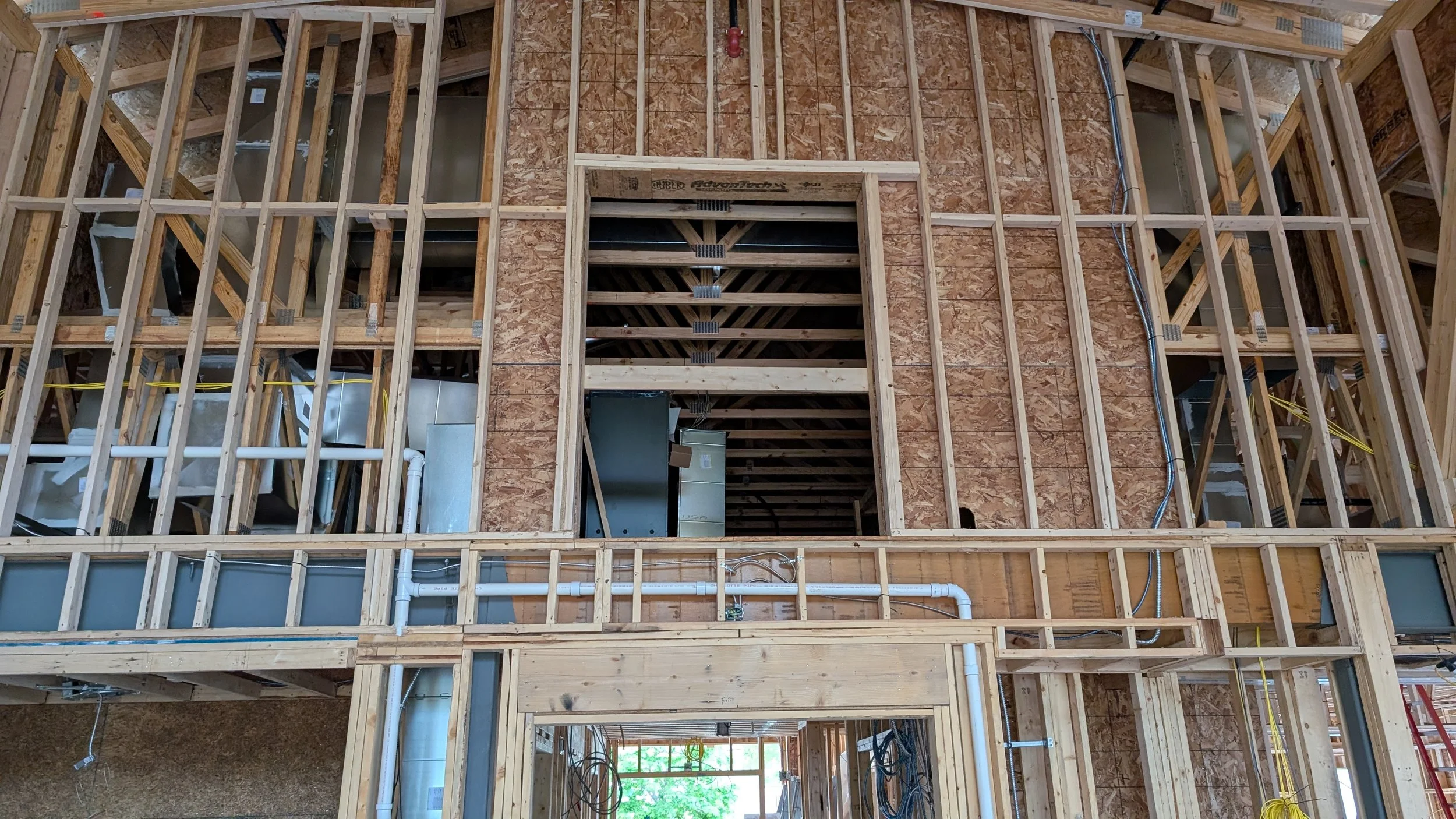 Construction site with exposed wooden framing and partially installed HVAC and electrical systems in a building under construction.
