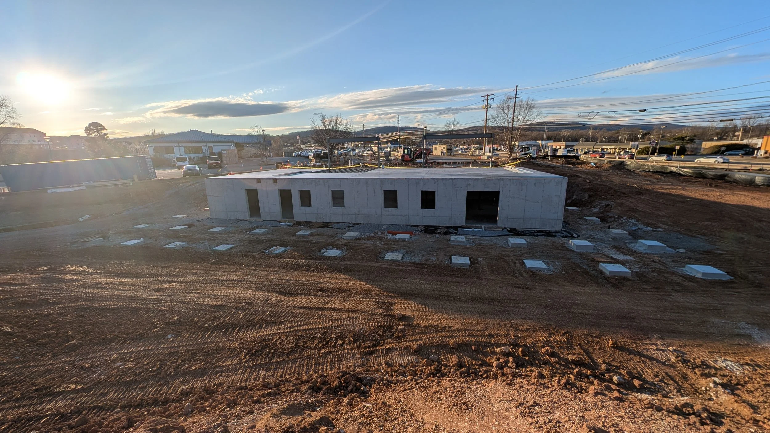 Construction site with a partly built concrete building and surrounding dirt ground, taken during late afternoon sunlight.