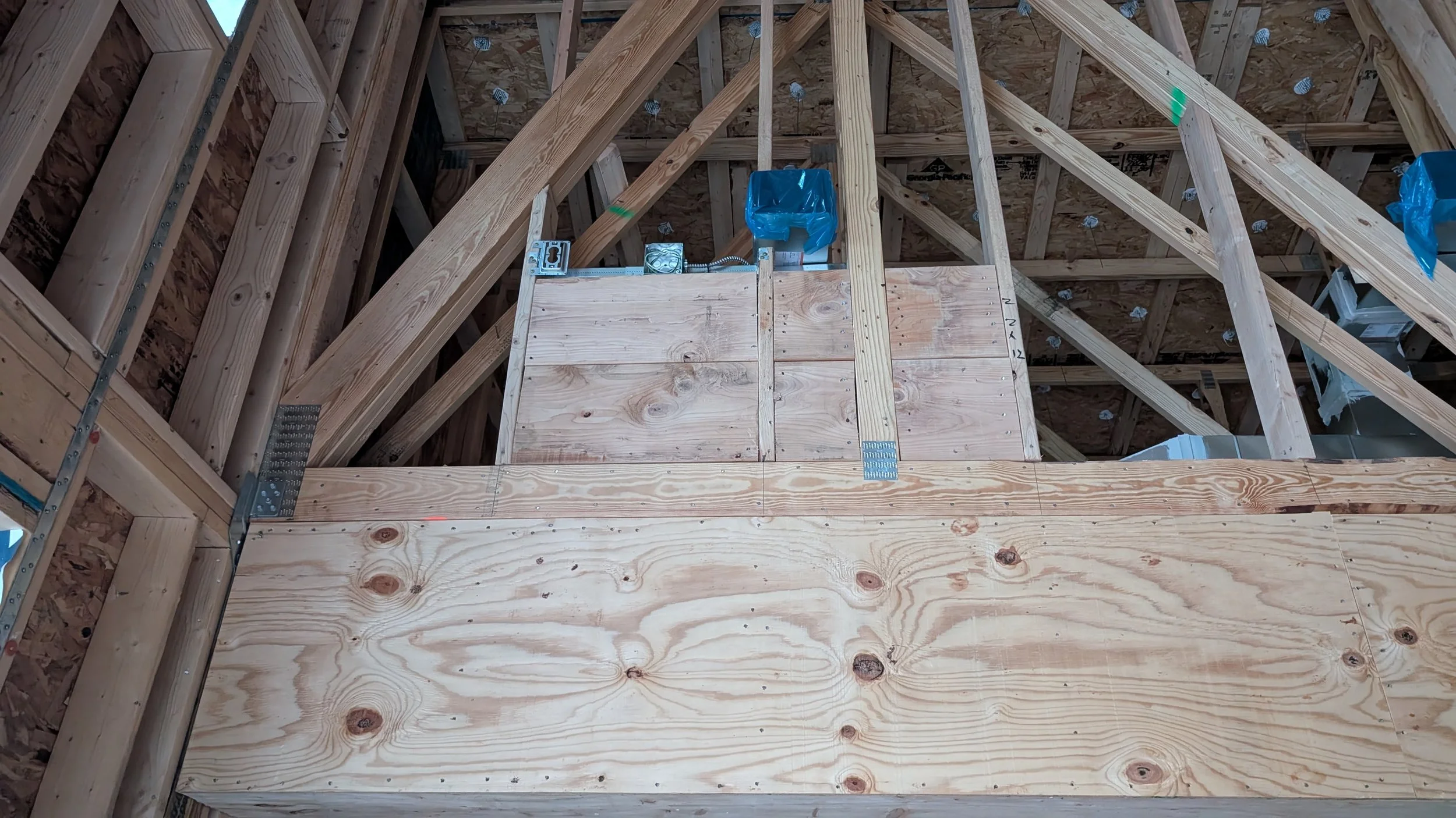 Interior view of a wooden construction site showing framing, plywood, and electrical wiring.