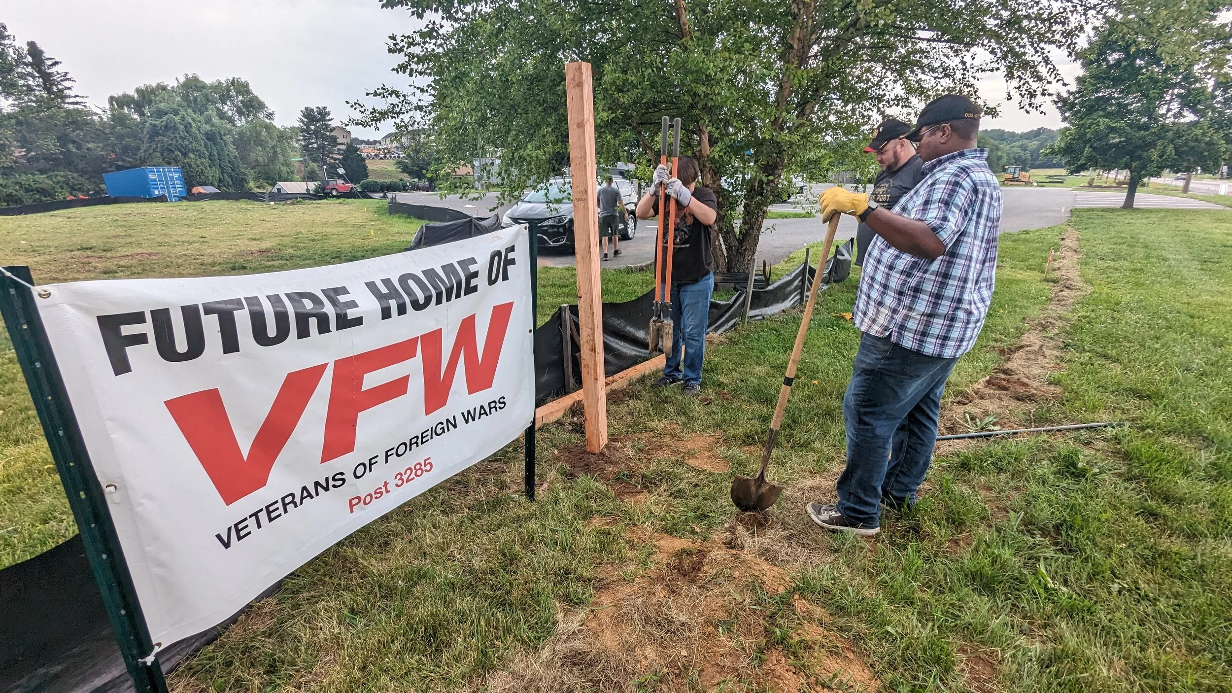 Group of people planting a tree in a grassy area, with a banner that reads 'Future Home of VFW Veterans of Foreign Wars Post 3285'.