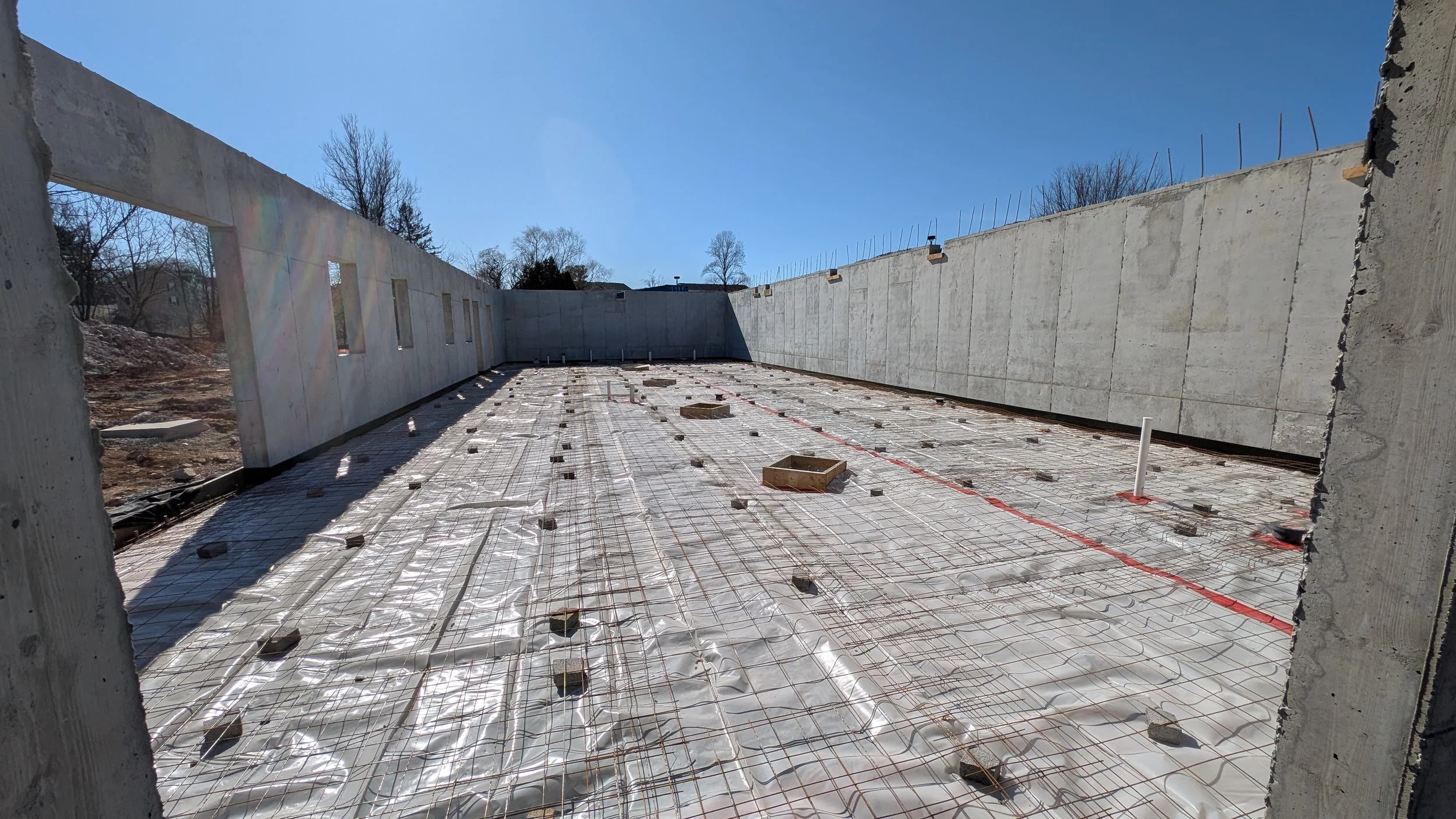 Construction site with concrete walls and rebar reinforcement on the ground, under a clear blue sky.