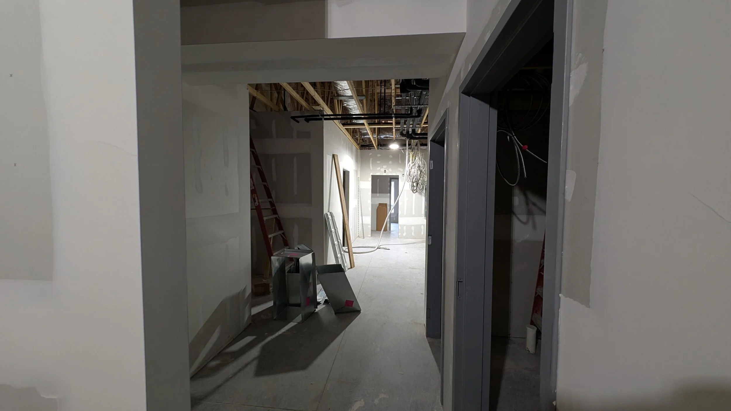 Construction site with unfinished walls, electrical wiring, and exposed ceiling framework, showing ongoing building work.