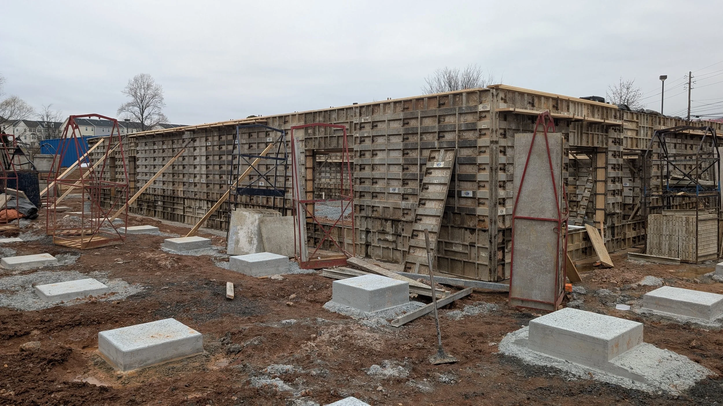 Construction site with wooden formwork for concrete walls, metal supports, steel rebar, and concrete footings on muddy ground.