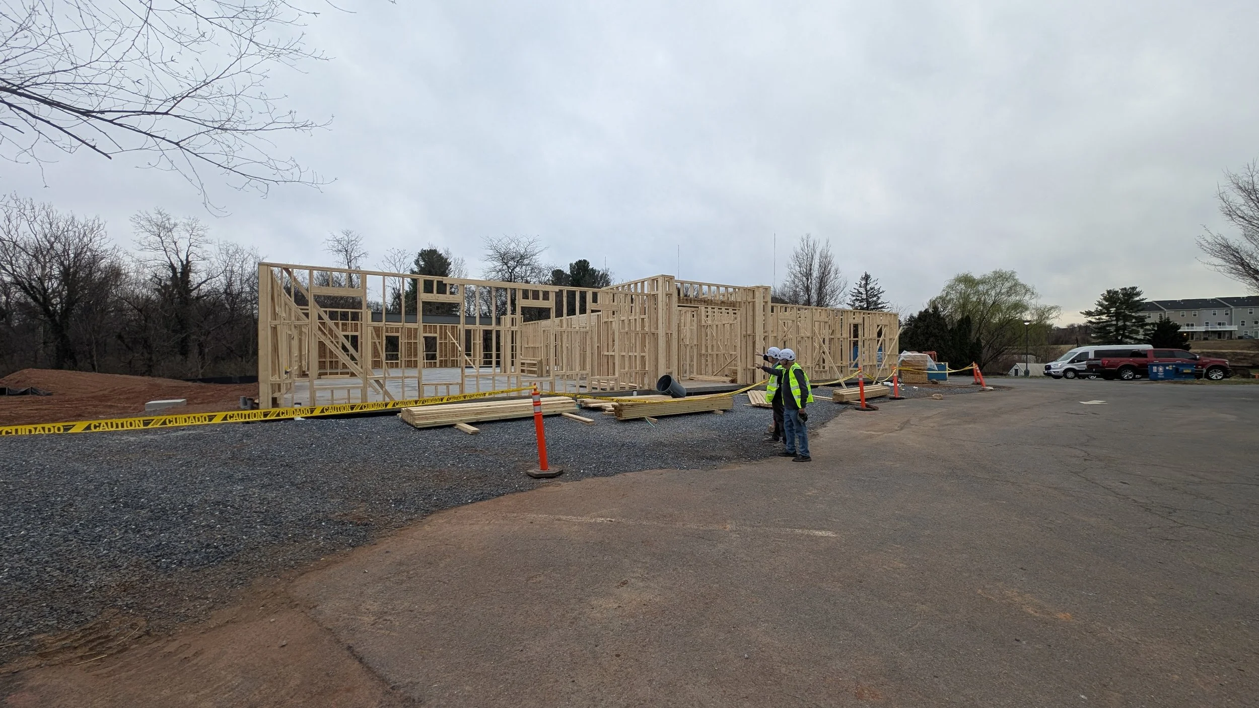 Construction site with wooden framing for a building, construction workers wearing helmets and safety vests, and caution tape around the area.